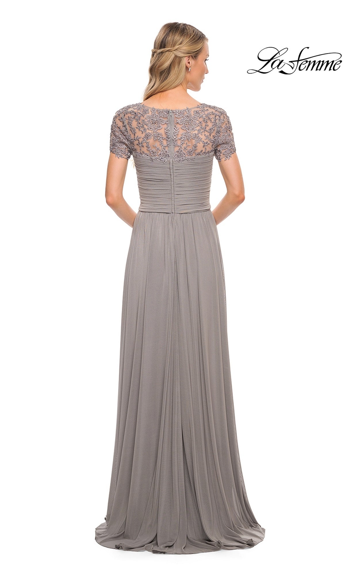 Woman in the Long Formal Dress: La Femme 29772—a floor-length taupe gown with an A-line skirt, short lace sleeves, and a ruched bodice—stands with her back to the camera.
