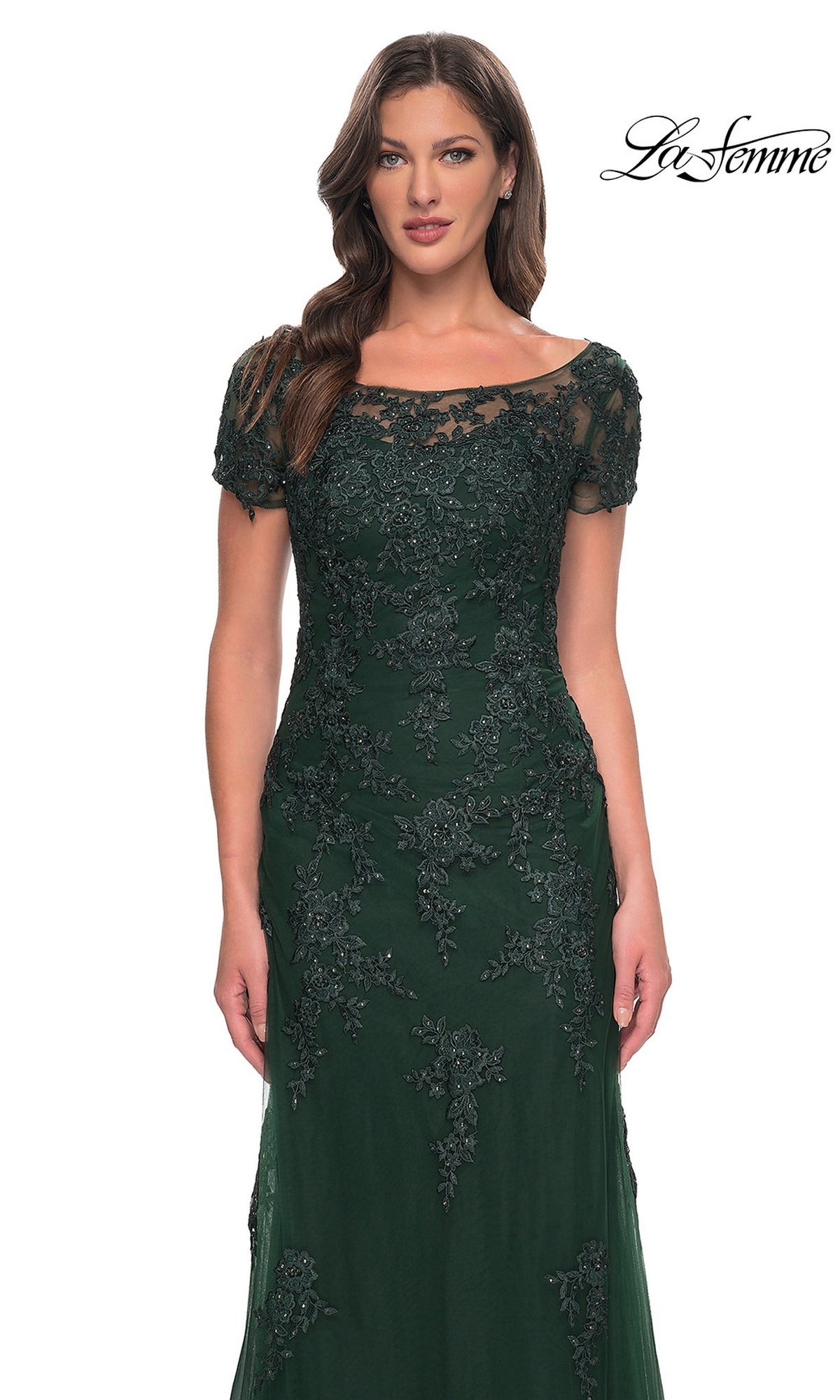 A woman wears the Long Formal Dress: La Femme 29792, a dark green, short-sleeved lace formal gown featuring an illusion neckline and intricate floral bead detailing.