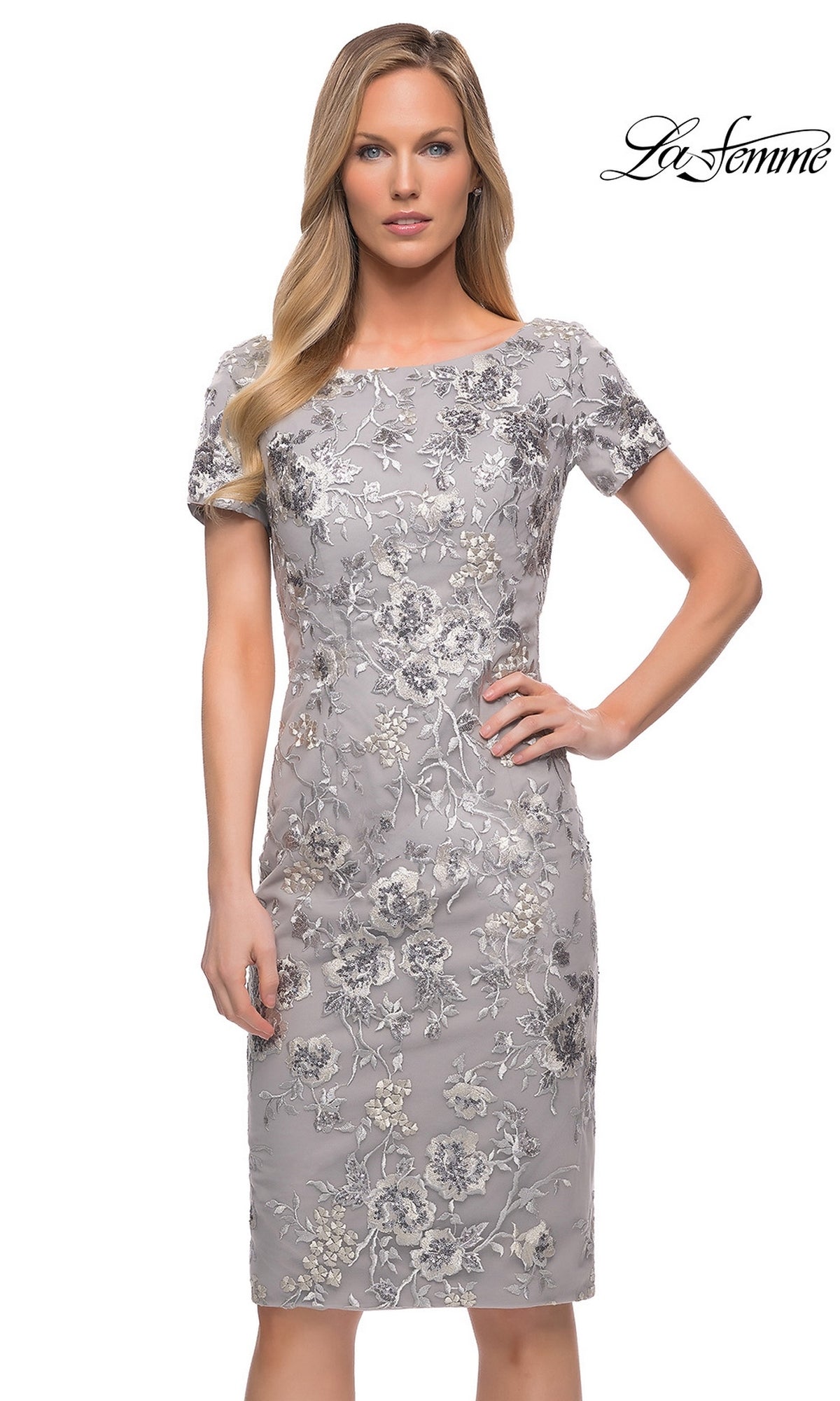 A woman models the Knee Length Wedding Guest Dress: La Femme 29824 with metallic floral-lace embroidery, posing in front of a plain white background. The โLa Femmeโ logo is top right.