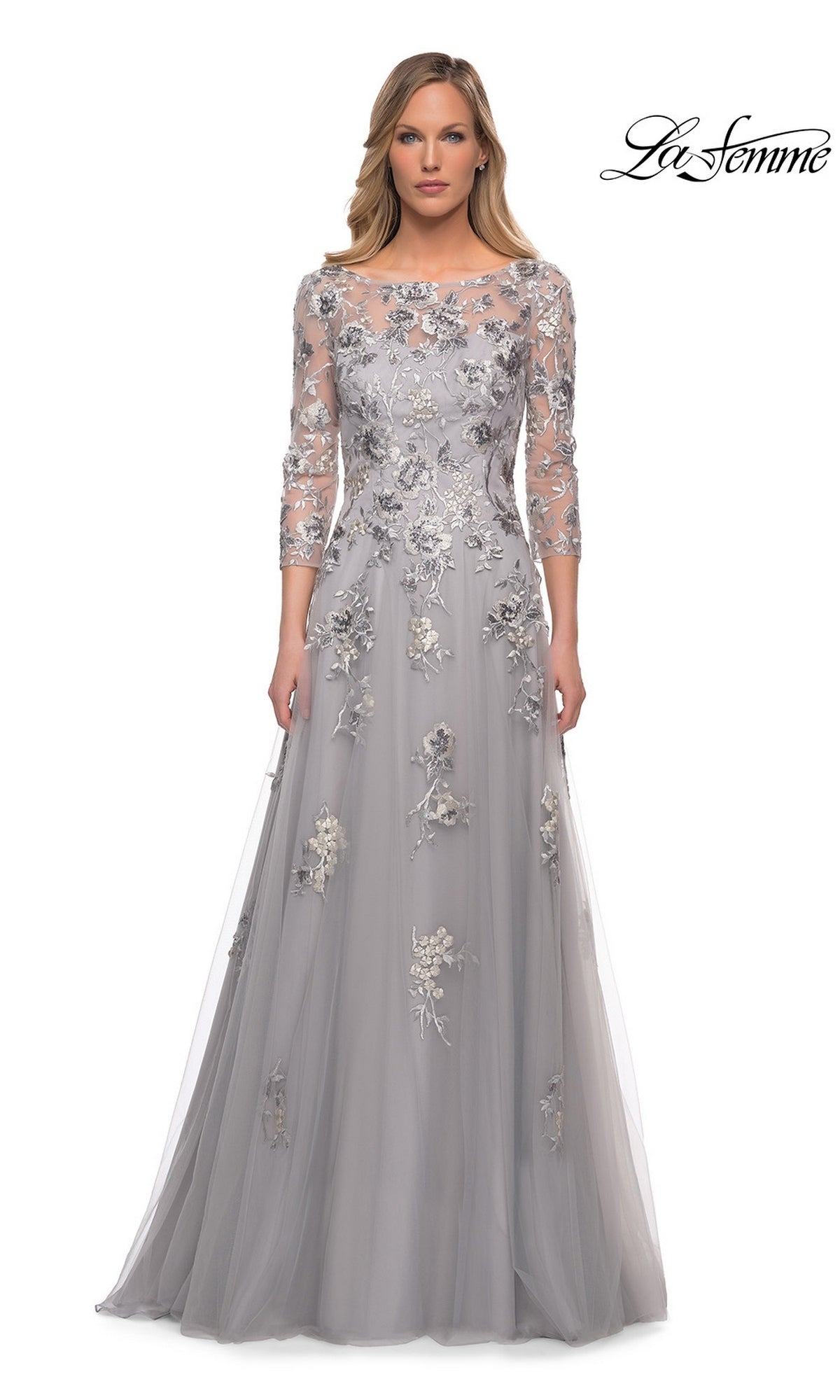 Woman wearing the Long Formal Dress: La Femme 29825, a silver-grey tulle gown with floral embroidery and sheer three-quarter sleeves, stands against a white background.