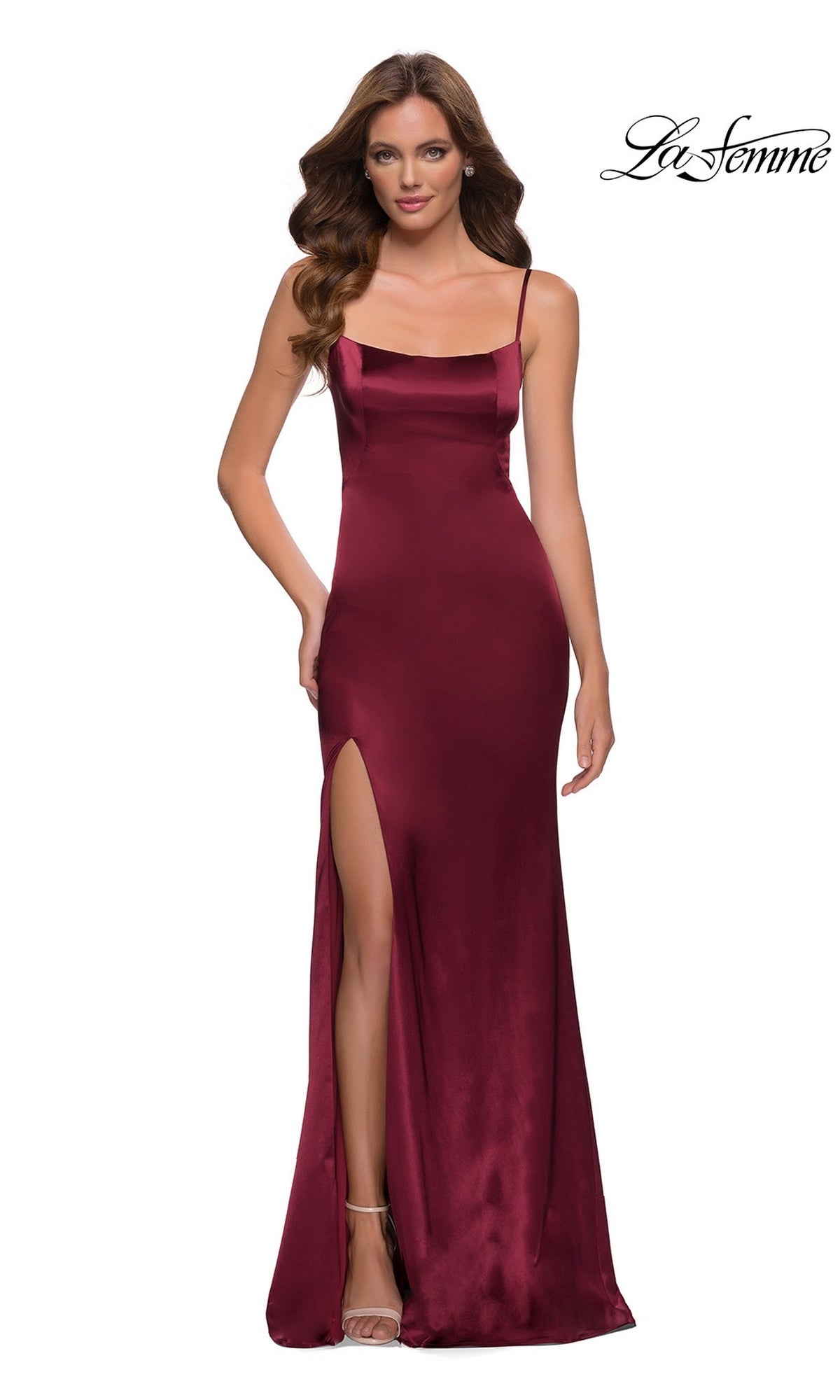 A woman stands against a white background wearing a burgundy La Femme Open-Back Simple Long Prom Dress 29945, which is sleeveless, floor-length, and features a thigh-high slit.