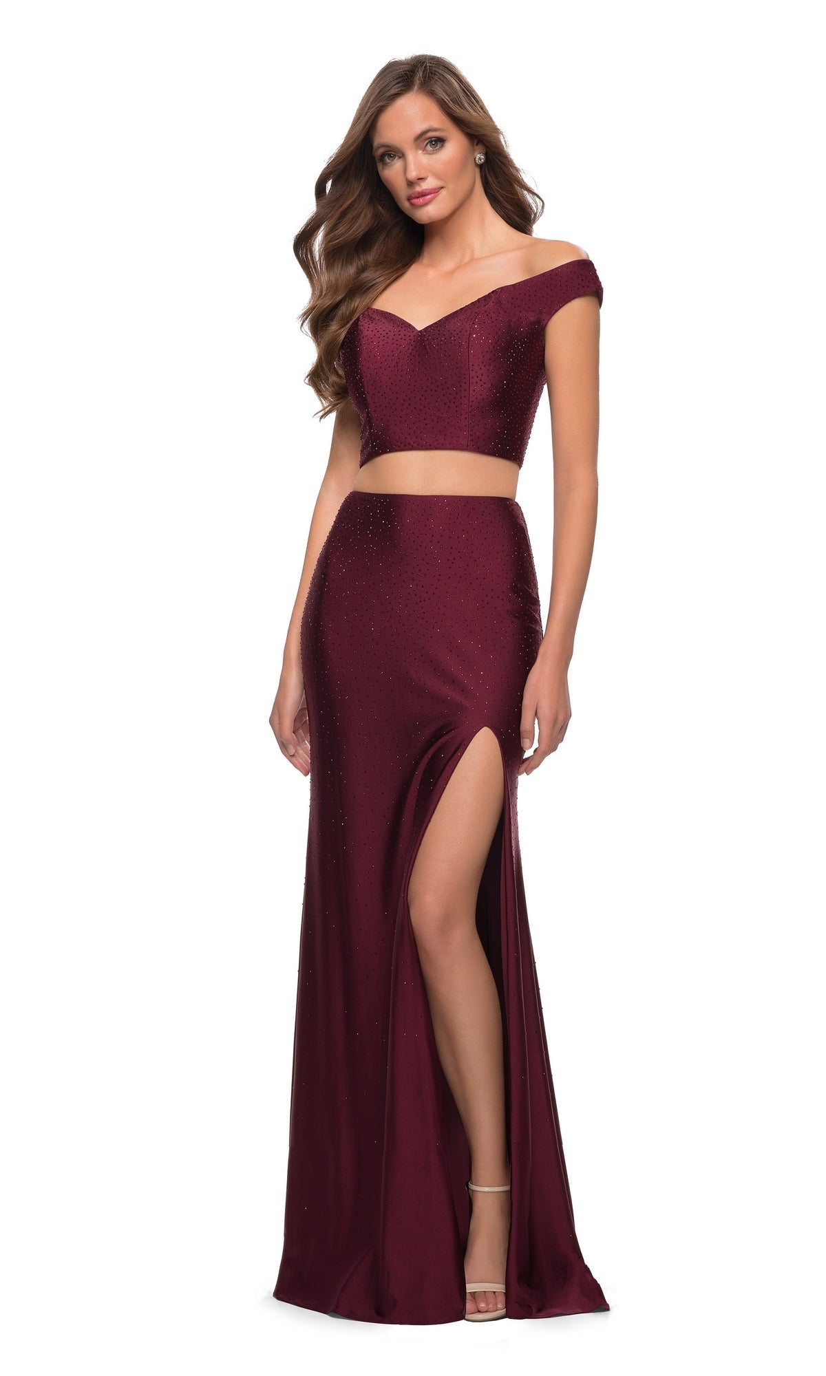 A woman stands facing forward in the Off-the-Shoulder Two-Piece Prom Dress: La Femme 29951, featuring a burgundy crop top and high-slit skirt, against a white background.