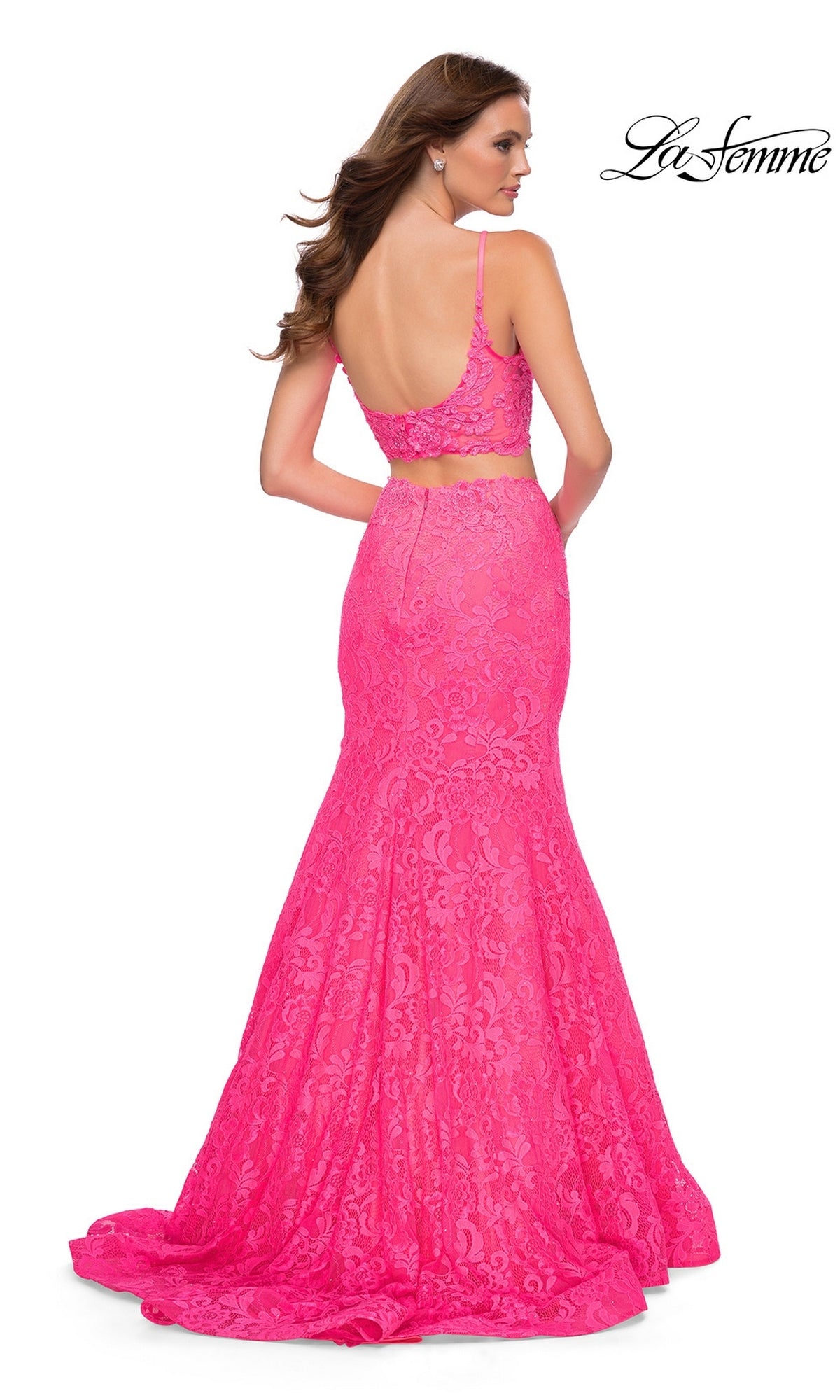 A woman wears a neon pink Long Prom Dress: La Femme 29967, featuring a two-piece lace formal gown with a cropped bodice and a floor-length mermaid skirt.
