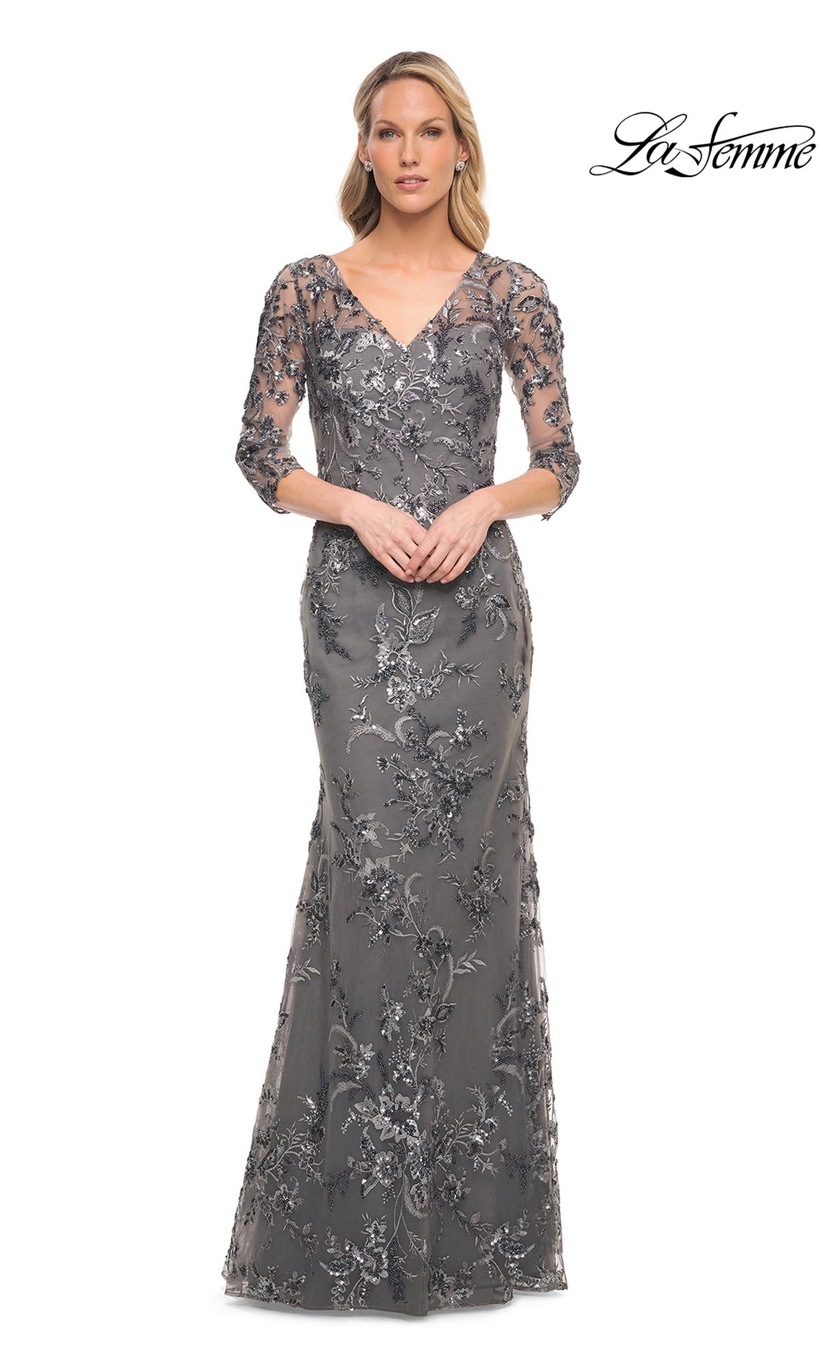 A woman wearing a Long Formal Dress: La Femme 29976, a modest, silver-grey, floor-length V-neck gown with three-quarter sleeves and silver floral embroidery.