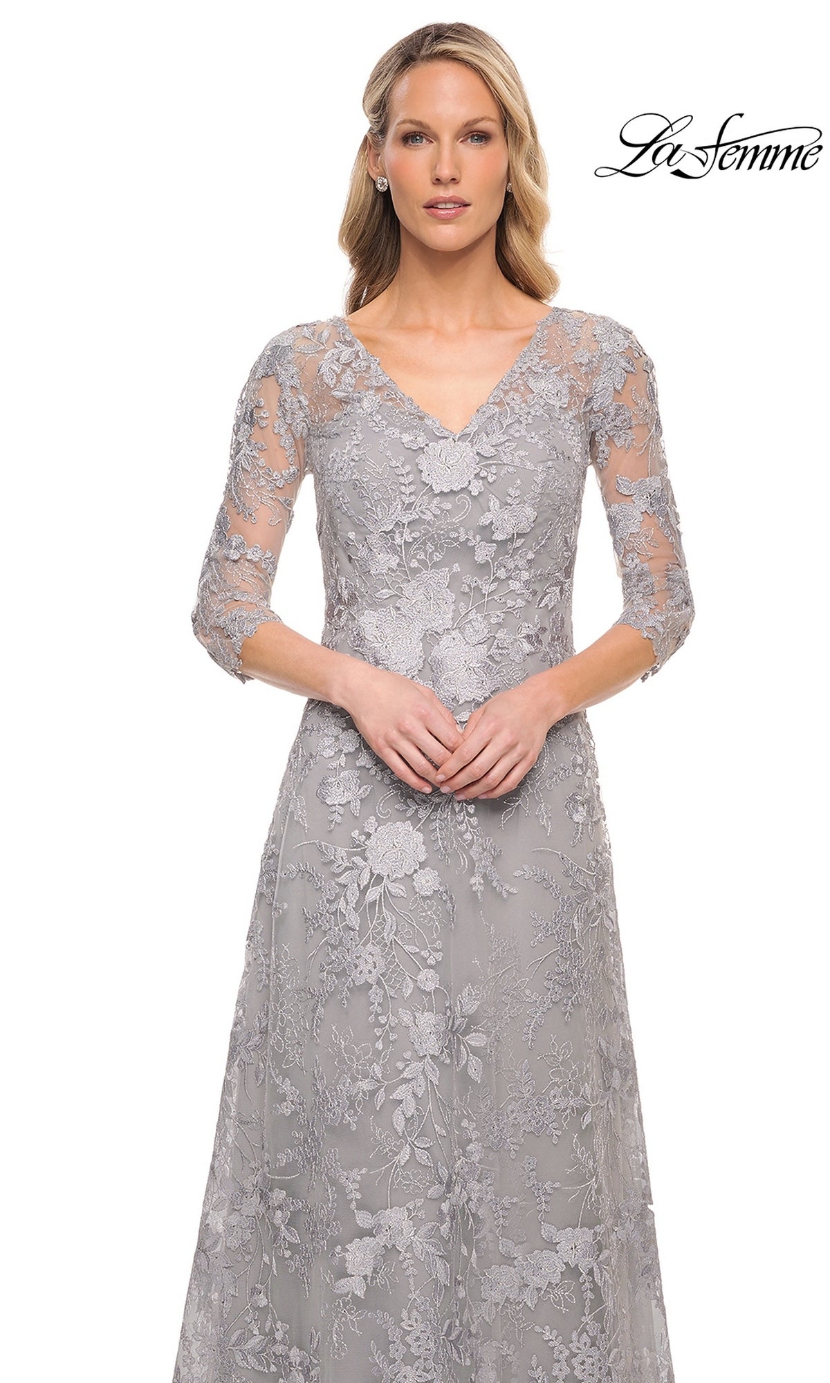 A woman wearing a silver, V-neck La Femme 29989 formal dress with three-quarter sleeves and floral lace embroidery.