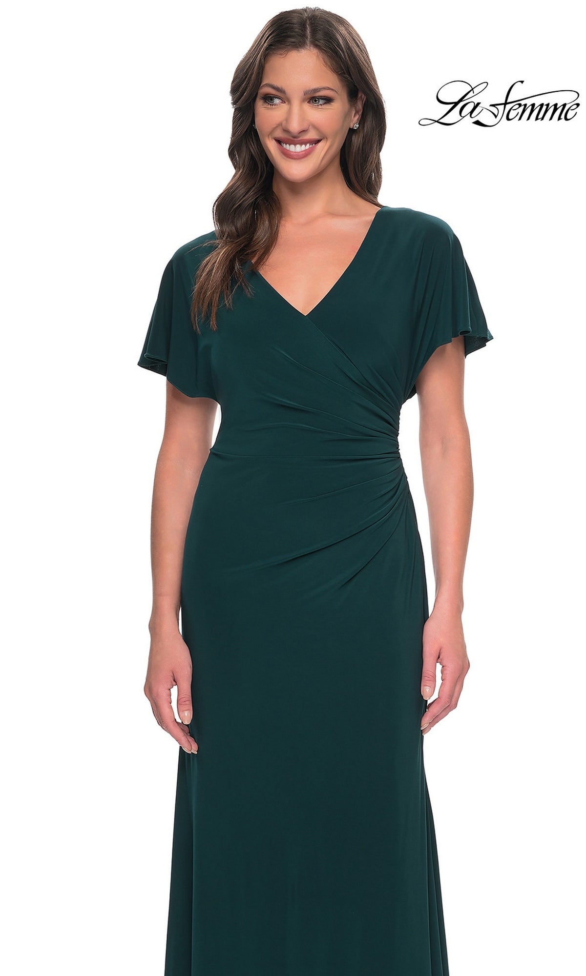 A woman wearing a La Femme 29997 long formal dress in dark green jersey, featuring a V-neckline, draped bodice, and short flutter sleeves.