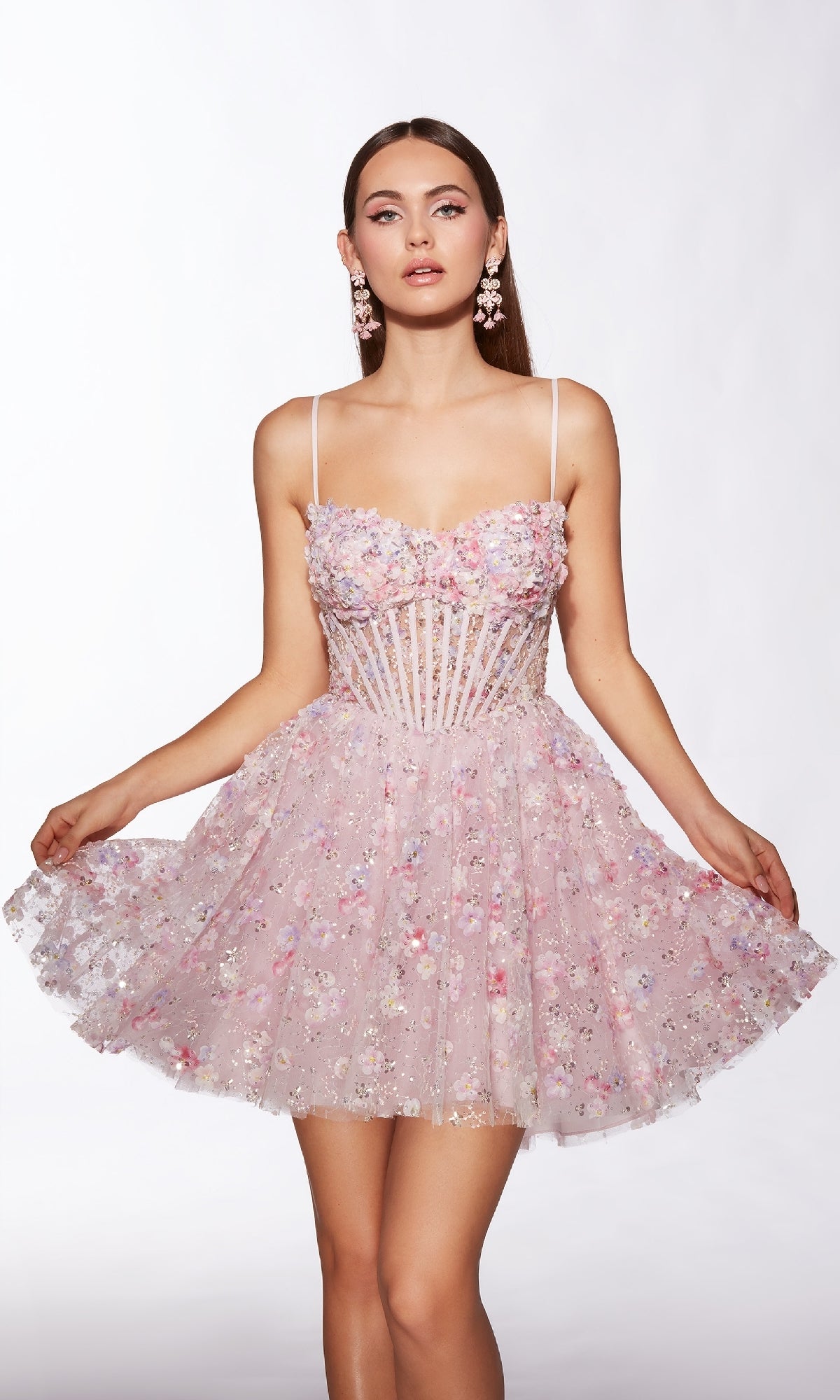 A woman models the Alyce 30003 short homecoming dress, a light pink fit-and-flare style with floral embroidery, sheer corset bodice, and thin straps, gently holding out the skirt against a plain background.