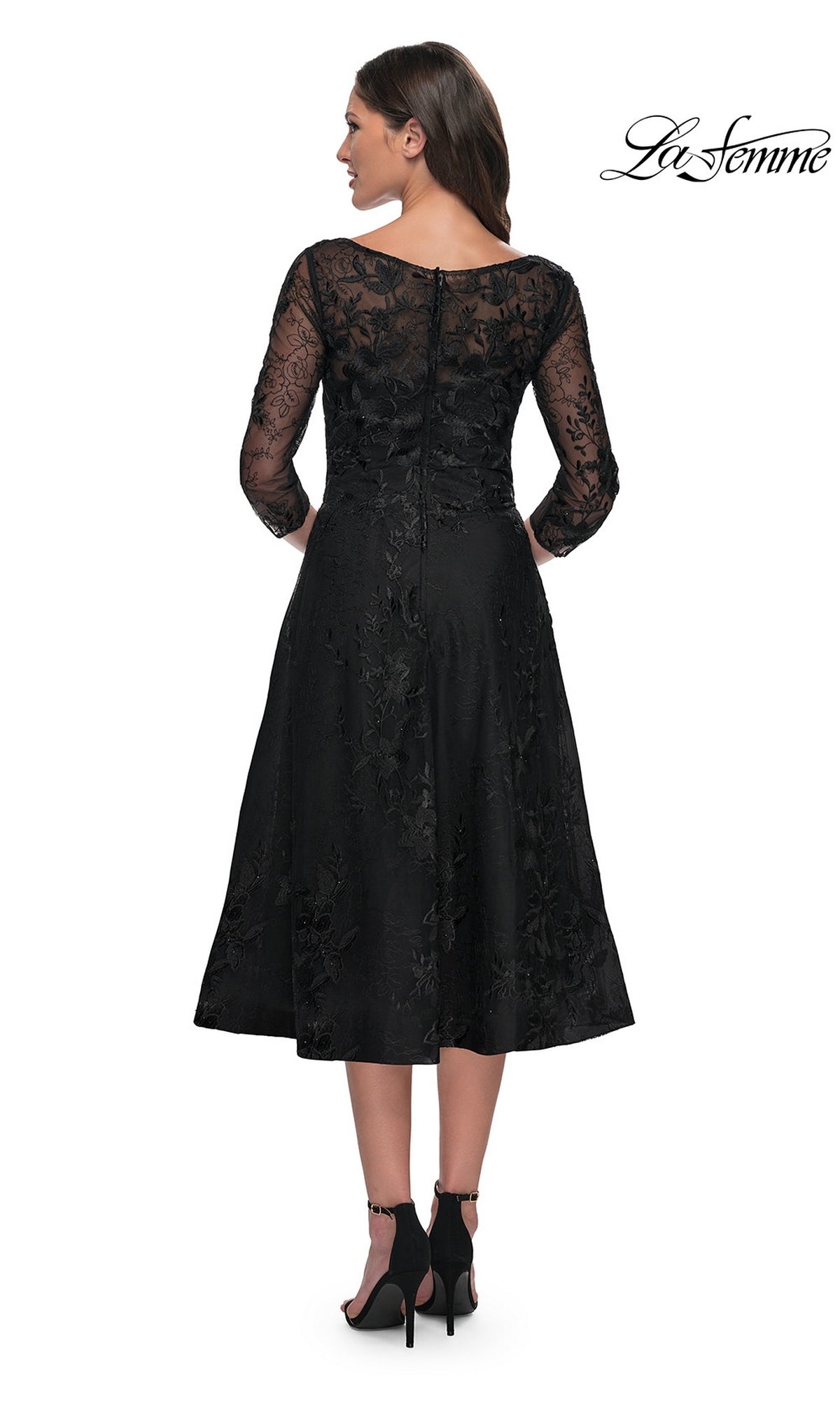 Back view of a woman wearing the Midi Wedding Guest Dress: La Femme 30016, a modest lace midi dress with sheer three-quarter sleeves, floral embroidery, and black high-heeled sandals.