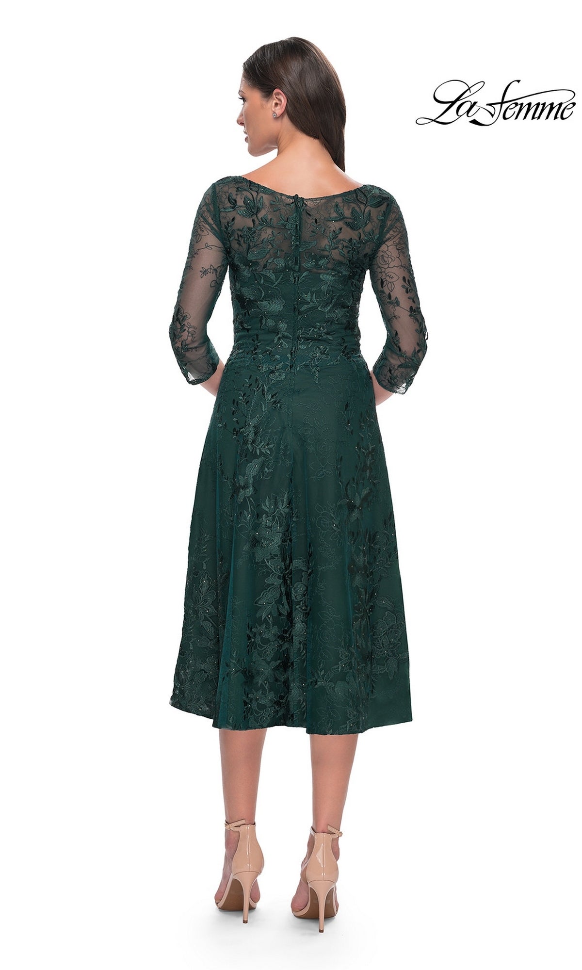A woman wearing a dark green, modest lace Midi Wedding Guest Dress: La Femme 30016 with three-quarter sleeves and floral embroidery, paired with nude high-heeled pumps.