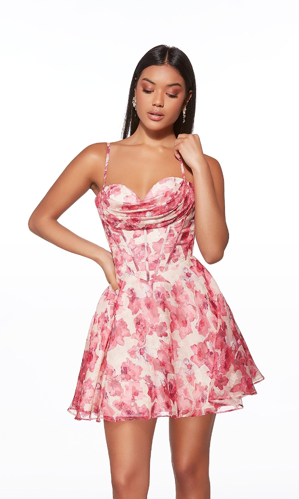 A woman wears the Alyce 30033 short homecoming dress featuring pink floral fabric, spaghetti straps, and a lace-up back, standing against a plain white background.