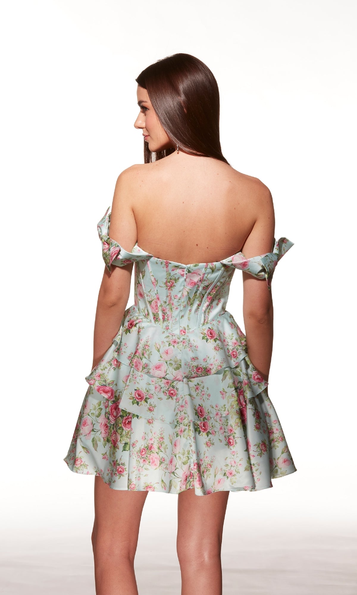 A woman faces away in the Alyce 30037 short homecoming dress—light blue with a pink floral pattern, off-shoulder neckline, fitted bodice, and flared skirt—against a plain white background.