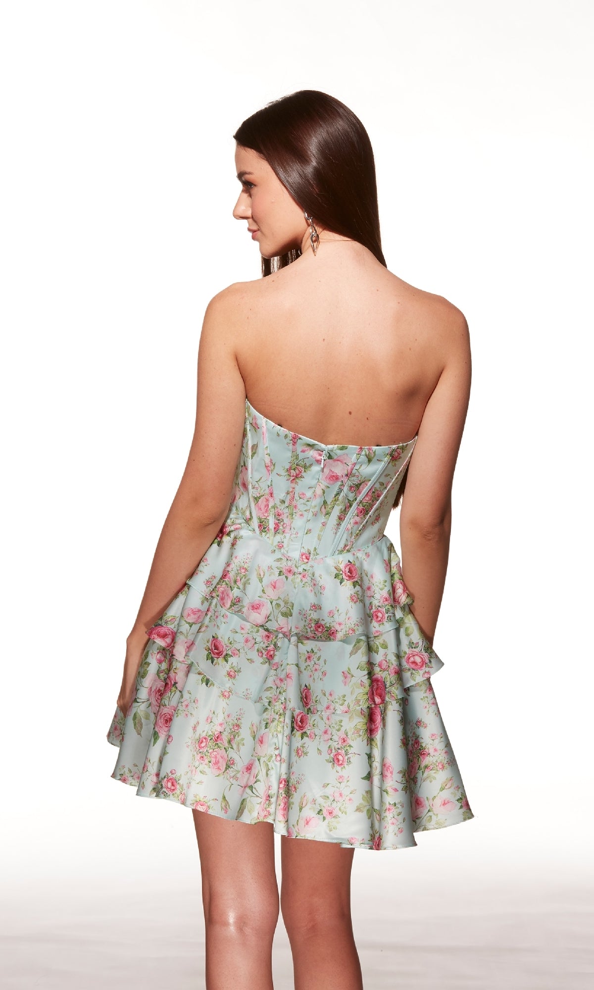 A woman wearing the Alyce 30037 short homecoming dress, featuring a floral pattern and fit-and-flare style, stands facing away to showcase the stylish back details against a plain white background.