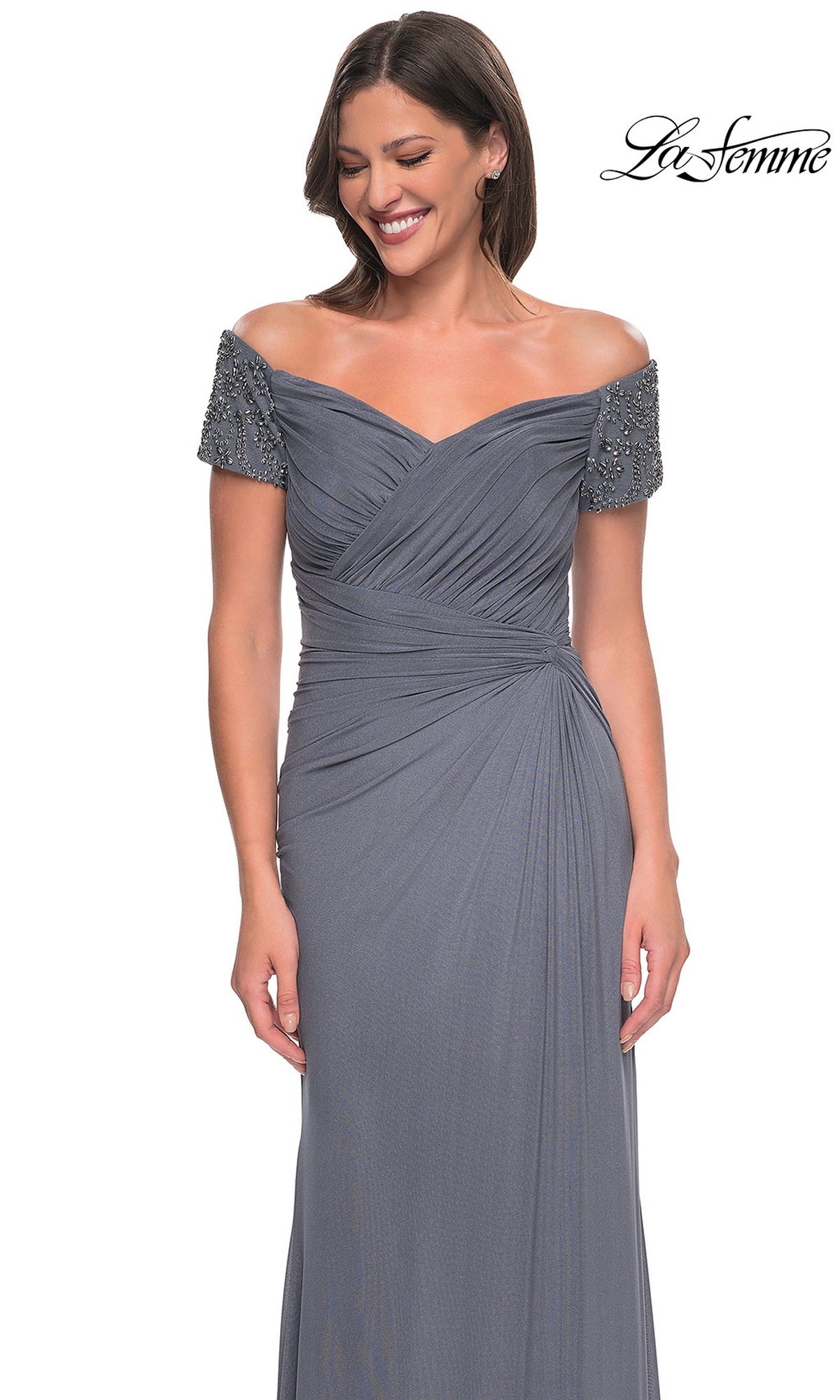 Woman in Long Formal Dress: La Femme 30057 featuring an off-the-shoulder beaded top, pleated bodice, and side-gathered skirt, standing and smiling. “La Femme” logo at top right.