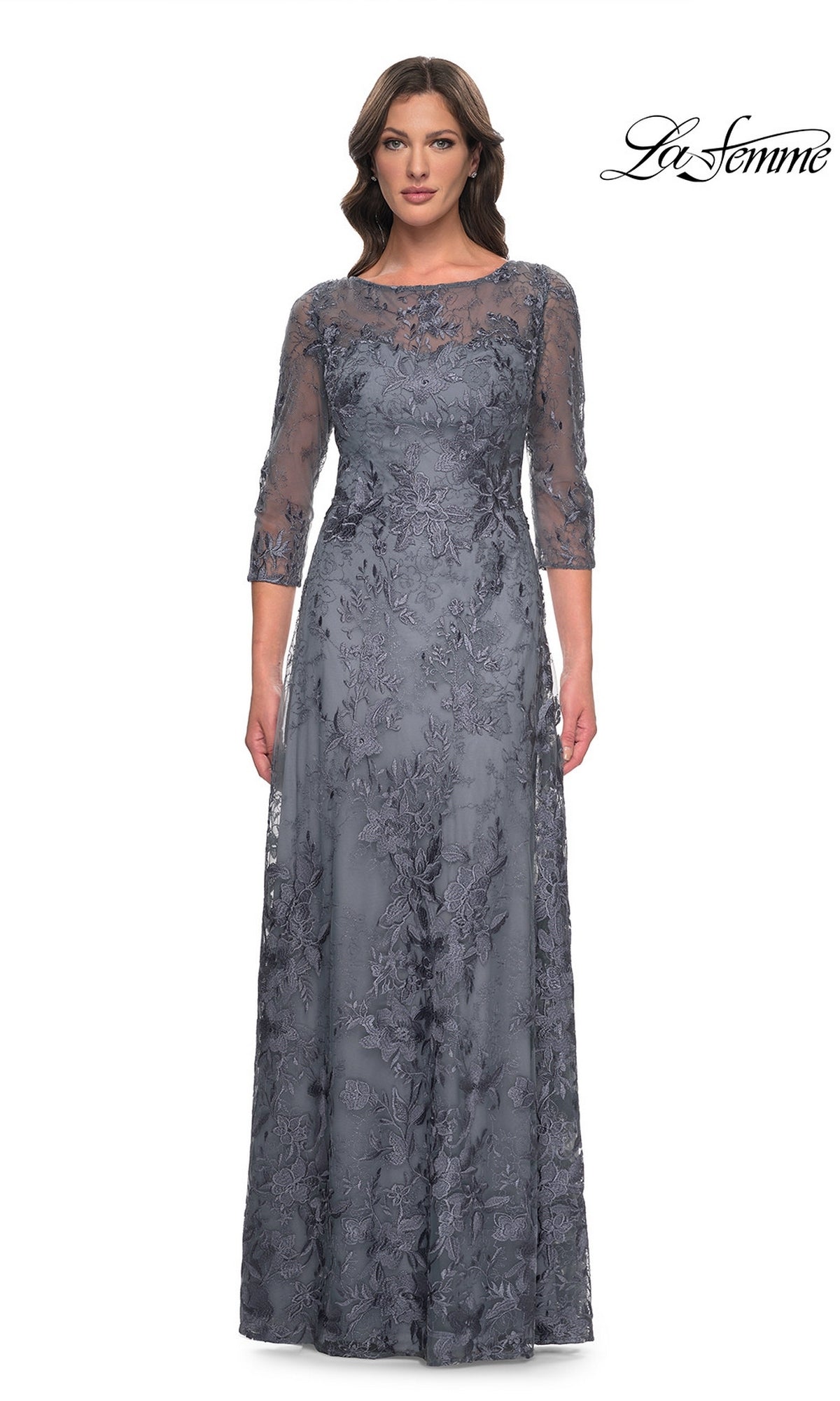 A woman wears a slate-colored La Femme 30060 long formal dress featuring a sheer lace overlay, three-quarter length sleeves, and a scoop neckline.