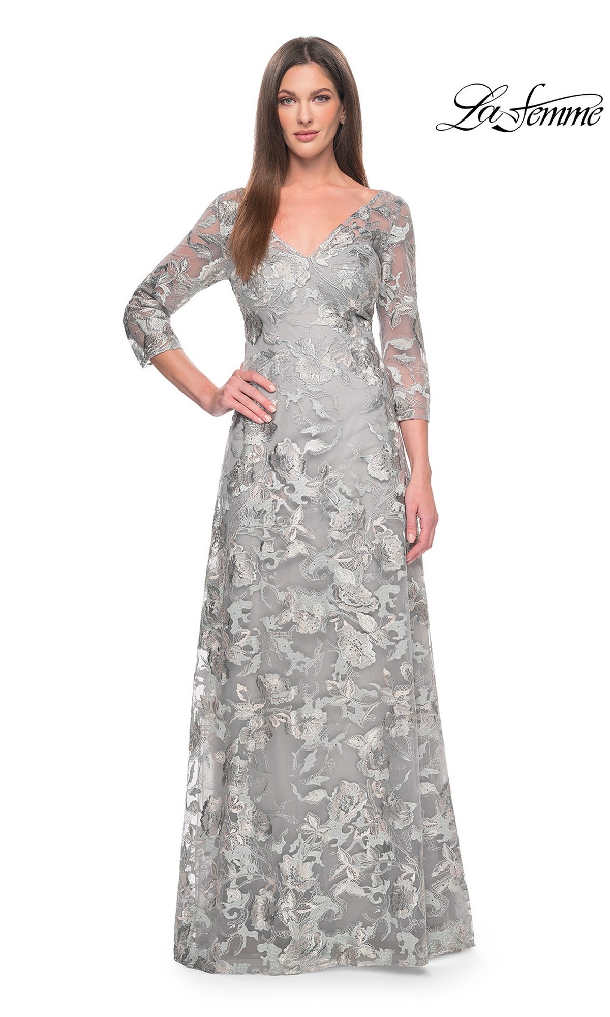 A woman wears a La Femme 30062 floor-length silver formal dress featuring a V-neck, three-quarter sleeves, and intricate metallic floral embroidery.