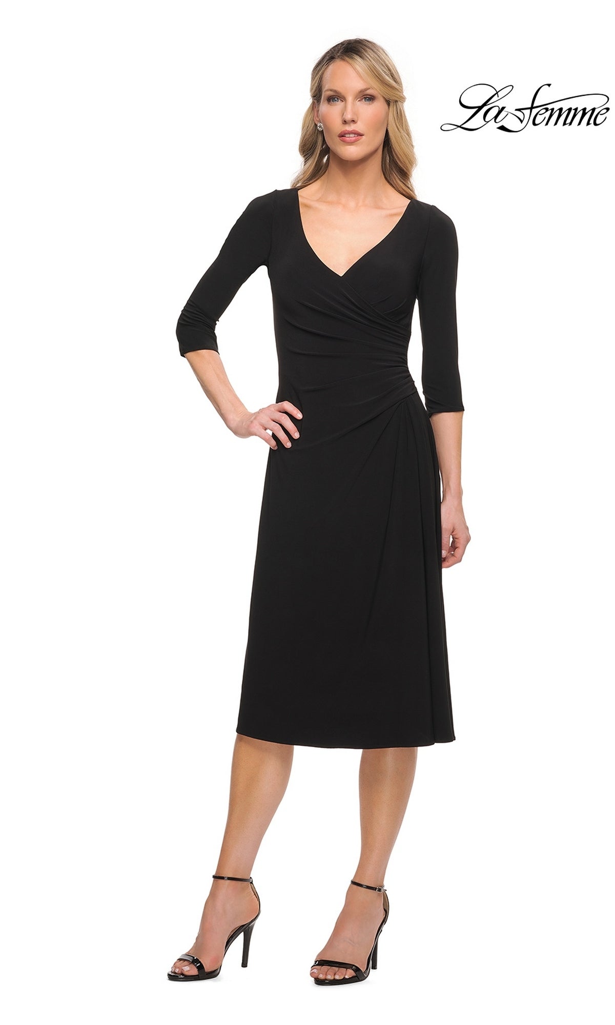 A woman wears a black, three-quarter sleeve Midi Wedding Guest Dress: La Femme 30069 featuring a V-neckline, side ruching, and black heeled sandals.