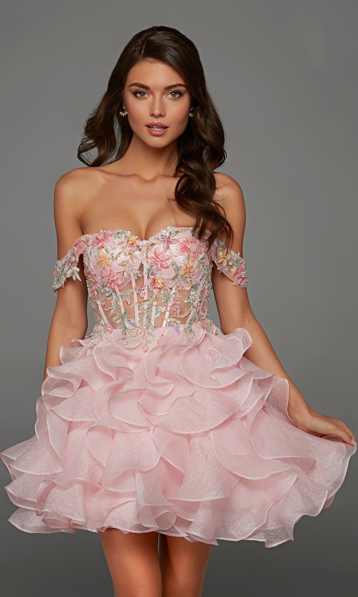 A woman wearing the Alyce 30087 short homecoming dress in Rosewater, featuring a fit-and-flare silhouette with a floral embroidered bodice embellished with delicate beaded floral appliques and a layered ruffled skirt, stands against a gray background.