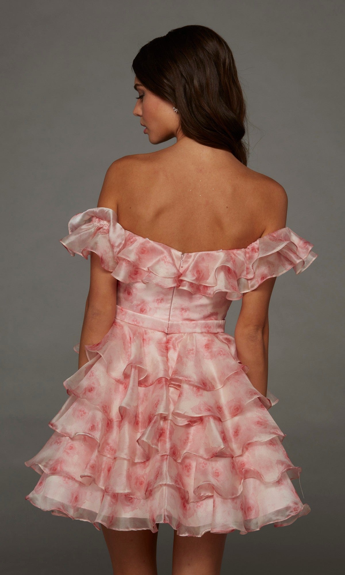 A woman facing away wears the Alyce 30089 short homecoming dress, featuring a ruffle tiered design with an off-shoulder pink and white layered skirt, set against a plain gray background.