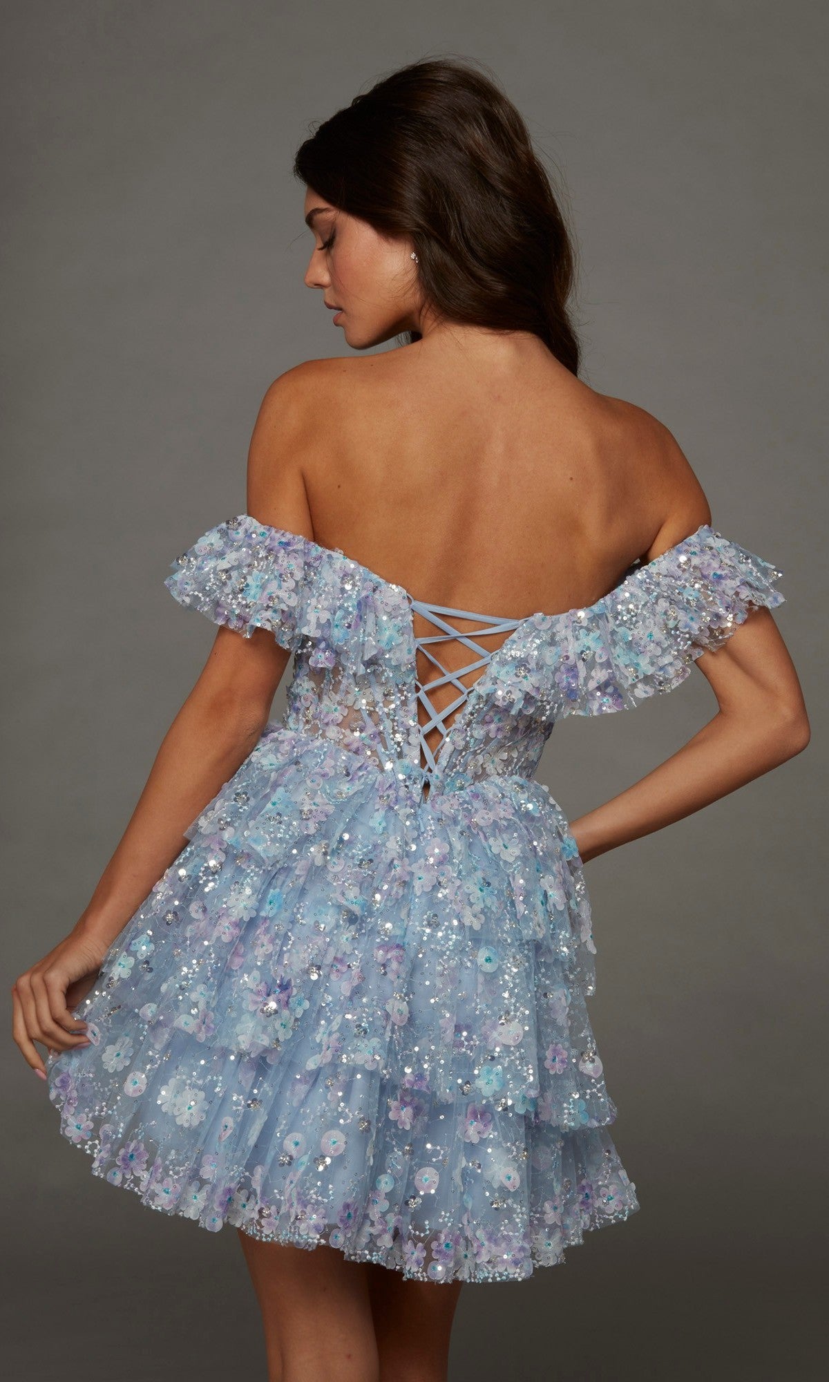 Wearing the Alyce 30115 short homecoming dress, a woman faces away in this light blue fit-and-flare party dress, which features off-shoulder ruffles, sequin floral detailing, and a lace-up back.