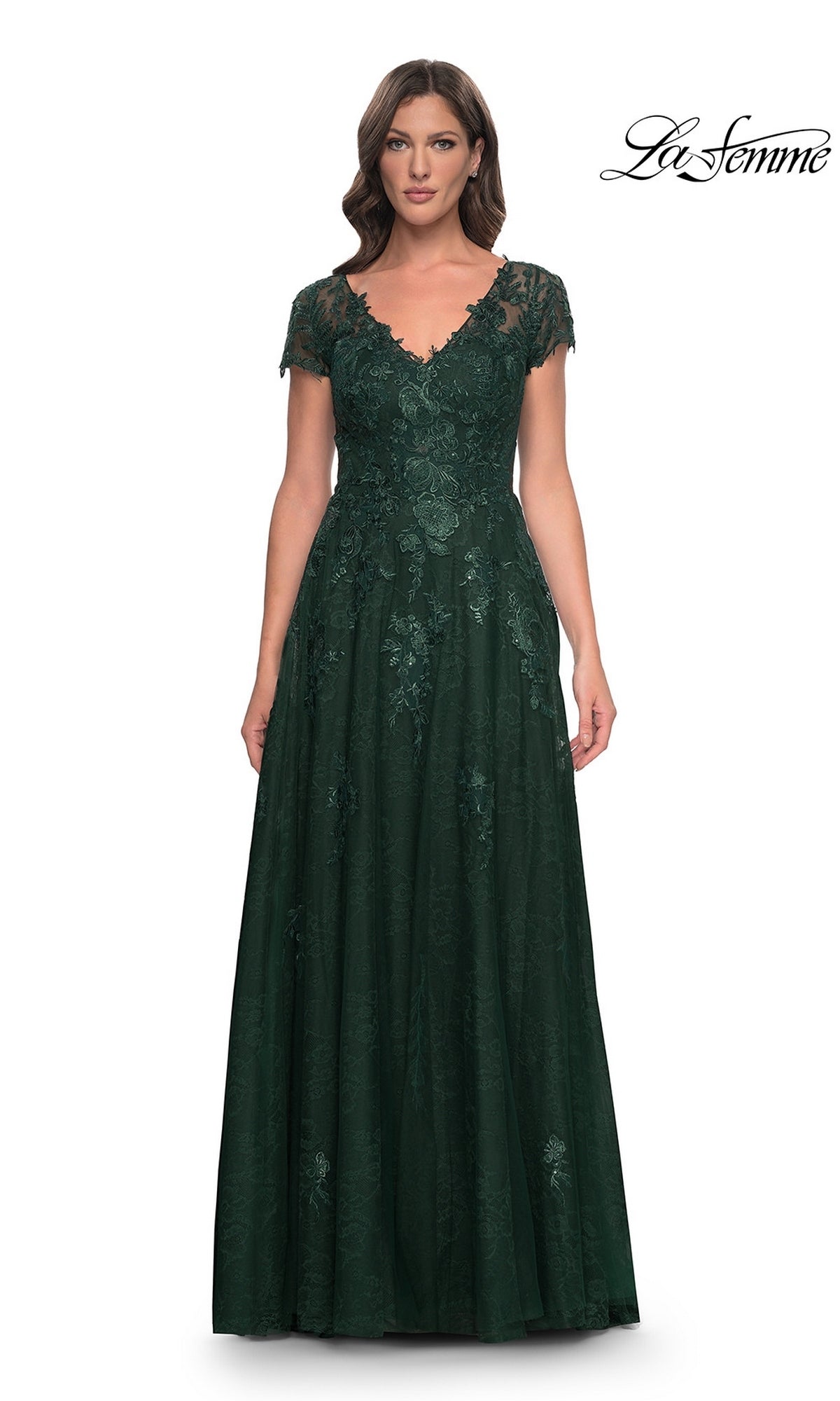 A woman wearing a floor-length, emerald green lace La Femme 30168 formal dress with short sleeves and a V-neckline.