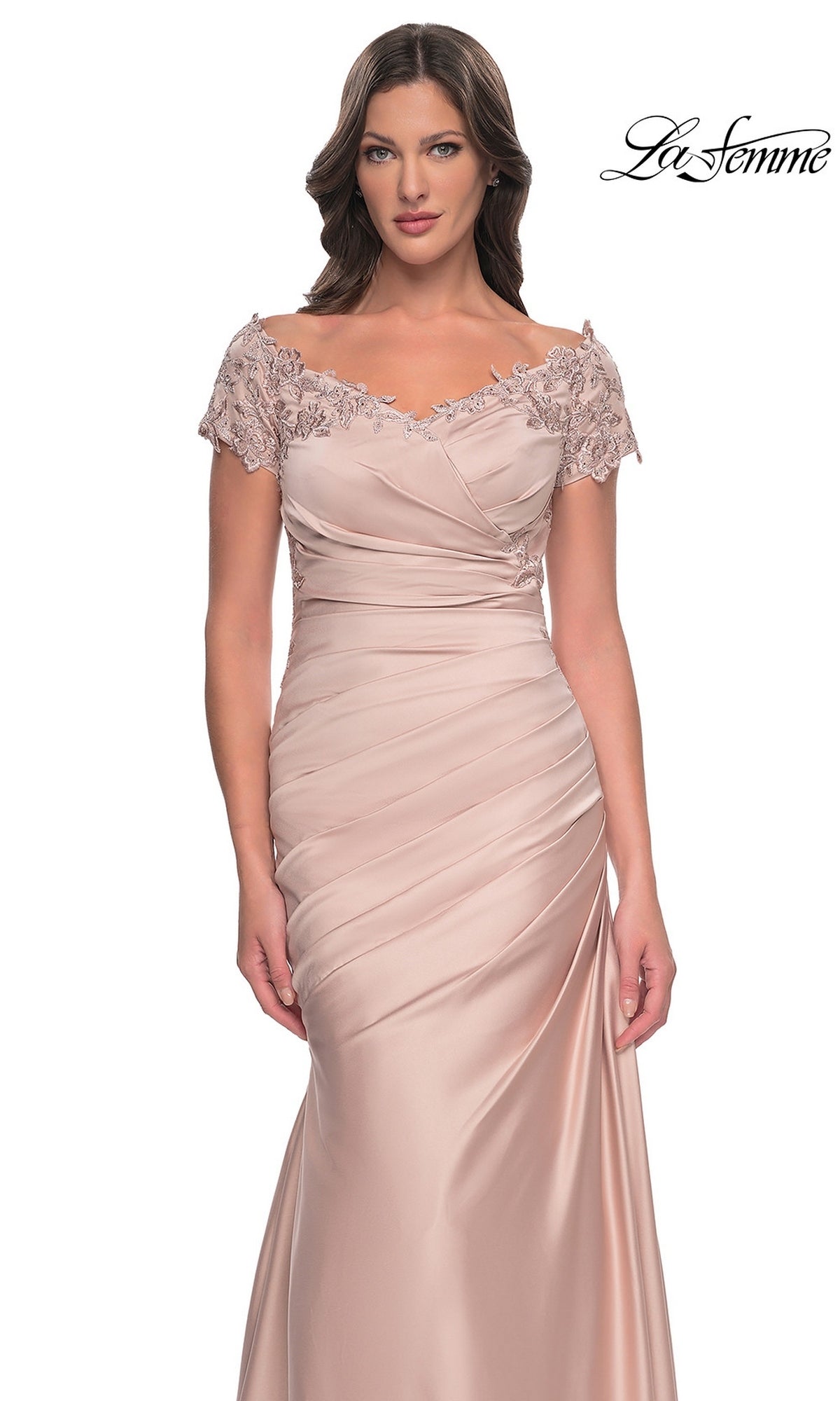 A woman wears a pale pink, long formal satin La Femme 30199 dress featuring an off-the-shoulder neckline, floral lace detailing, a ruched bodice, and a mermaid silhouette.
