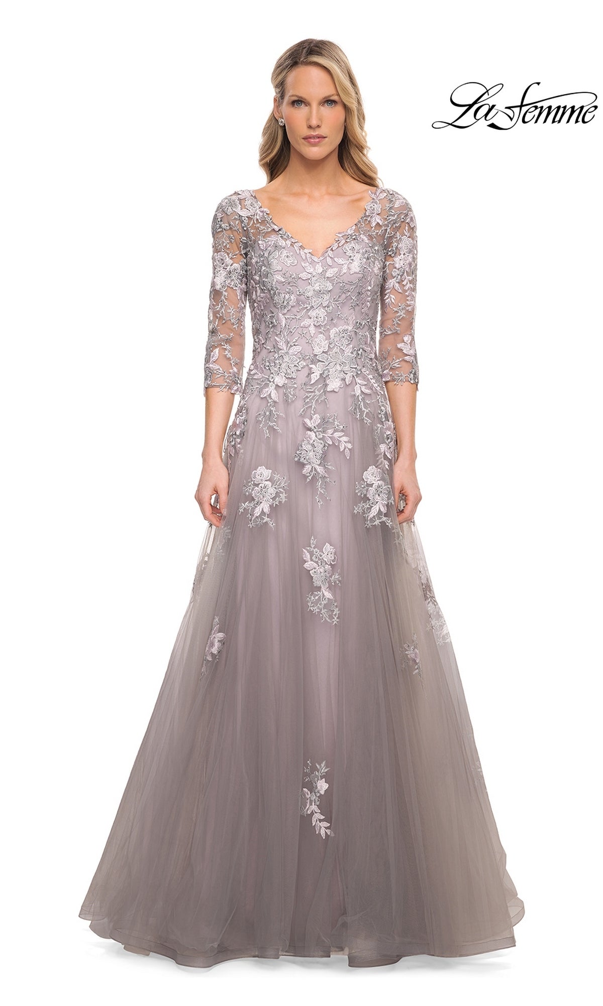 A woman wears the Long Formal Dress: La Femme 30229, a silver gown with three-quarter sleeves and floral lace appliques on the bodice and skirt.