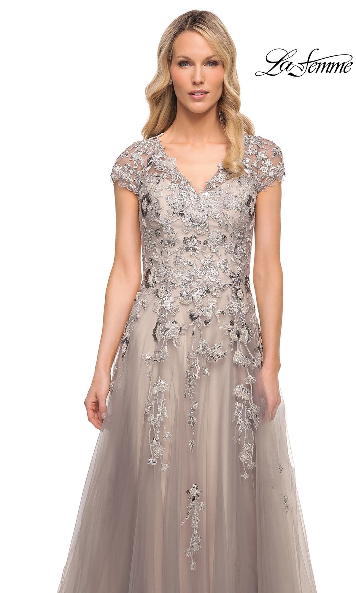 A woman wears a La Femme 30239 silver formal tulle A-line gown with a V-neckline, cap sleeves, and gray floral embroidery with sequins.