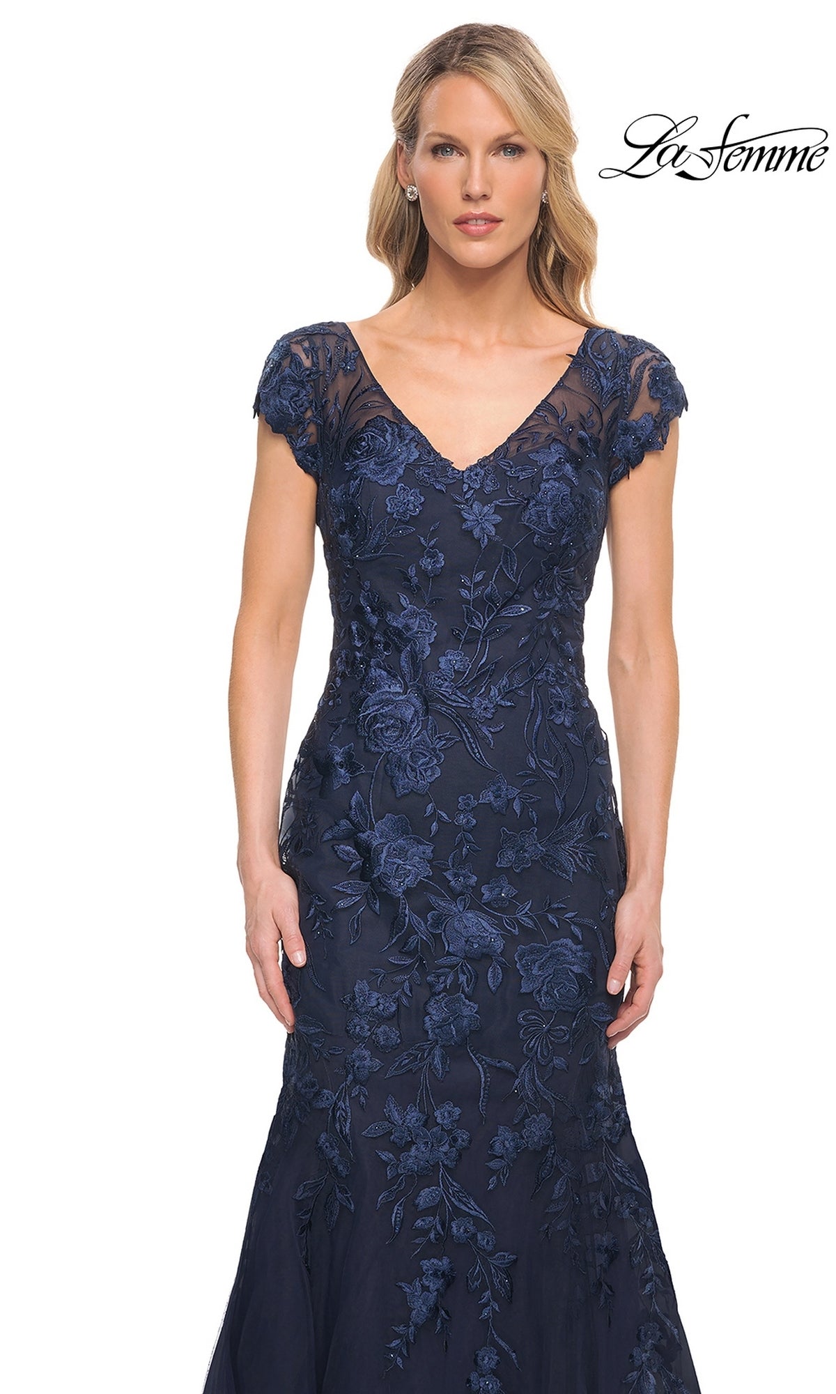 A woman wearing a La Femme 30269 floor-length navy blue mermaid silhouette dress with a V-neckline, cap sleeves, and floral embroidery.