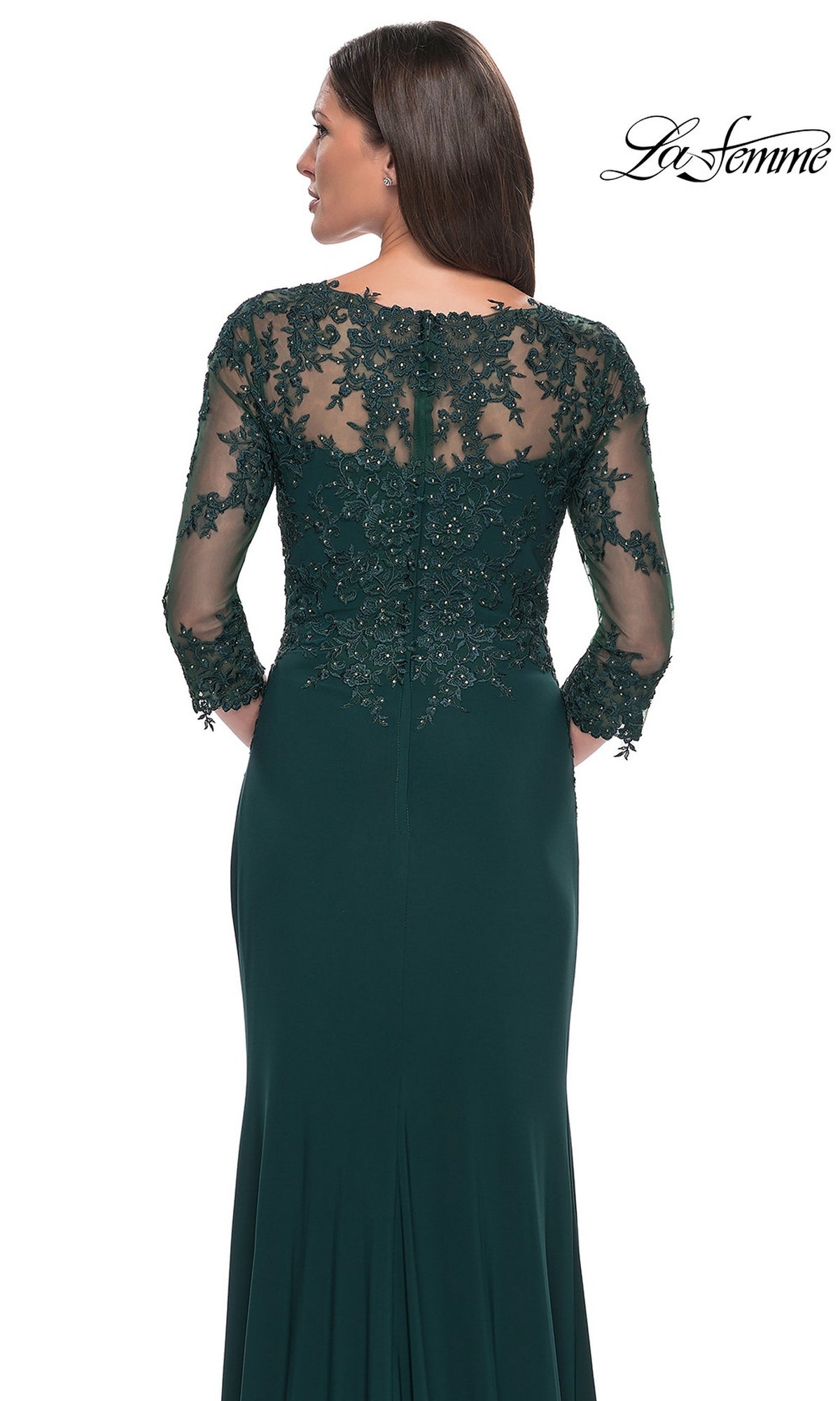 A woman wearing the Long Formal Dress: La Femme 30384, a dark green, floor-length gown with sheer lace sleeves and back detailing, faces away from the camera.