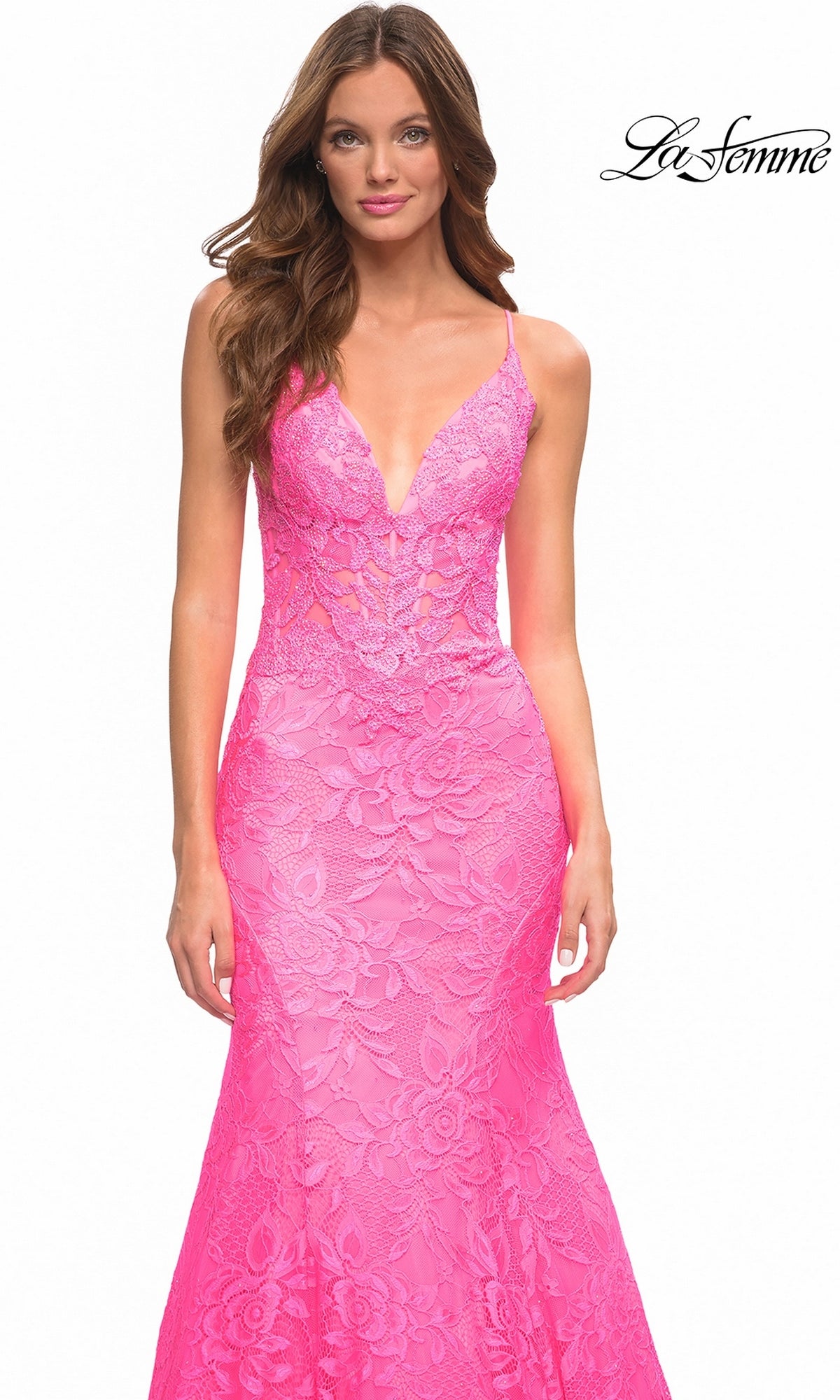 A woman wears a bright, hot pink La Femme 30663 mermaid prom dress in floor-length floral lace with a plunging V-neckline and spaghetti straps.