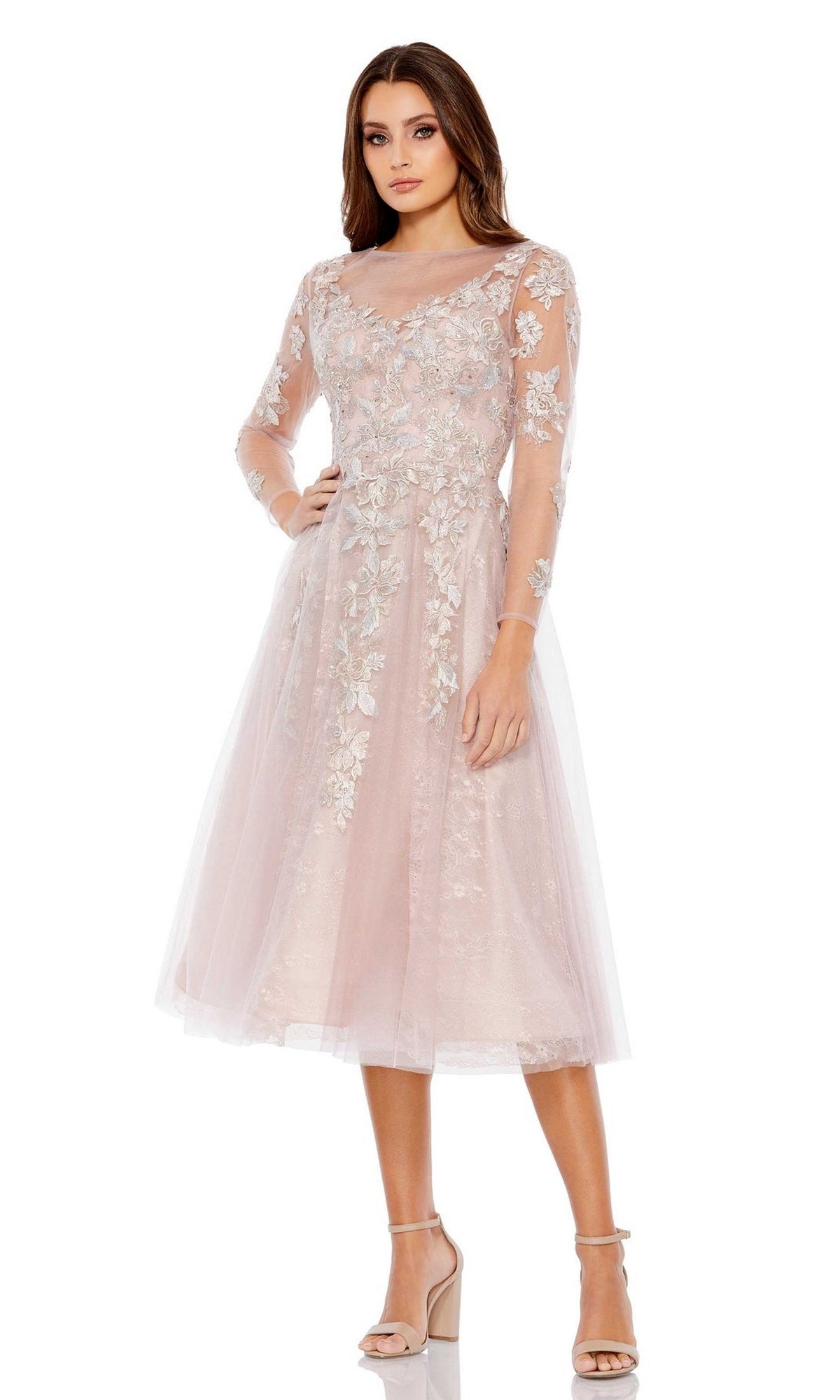 A woman stands in heels against a white background, wearing the Mac Duggal Short Wedding Guest Dress 30681—a knee-length blush pink A-line dress featuring long sheer sleeves and floral embroidery.