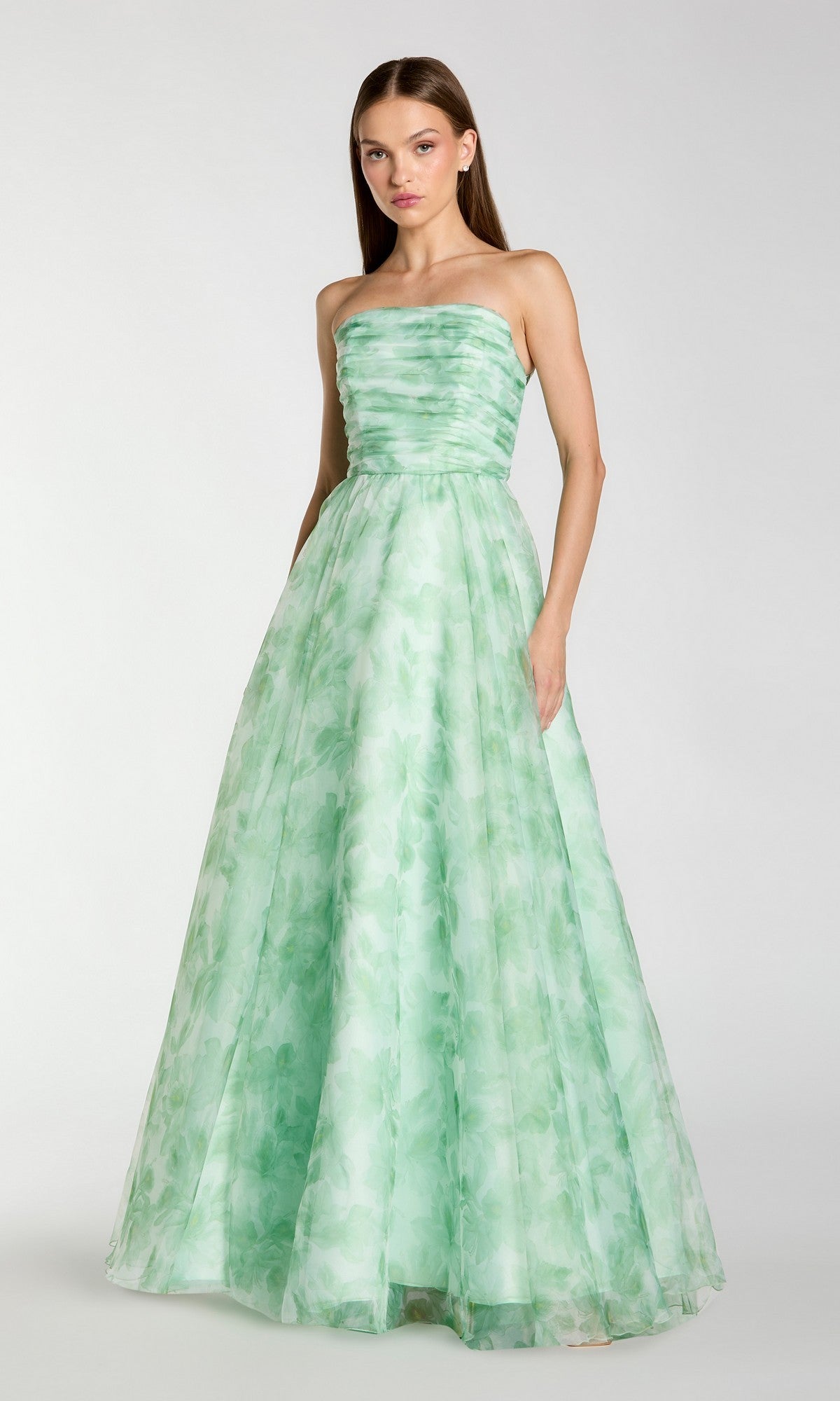 A woman stands facing forward, one hand in her pocket, wearing the Mac Duggal 30783 long formal dress—a strapless green evening gown with a ruched bodice and subtle leaf pattern.