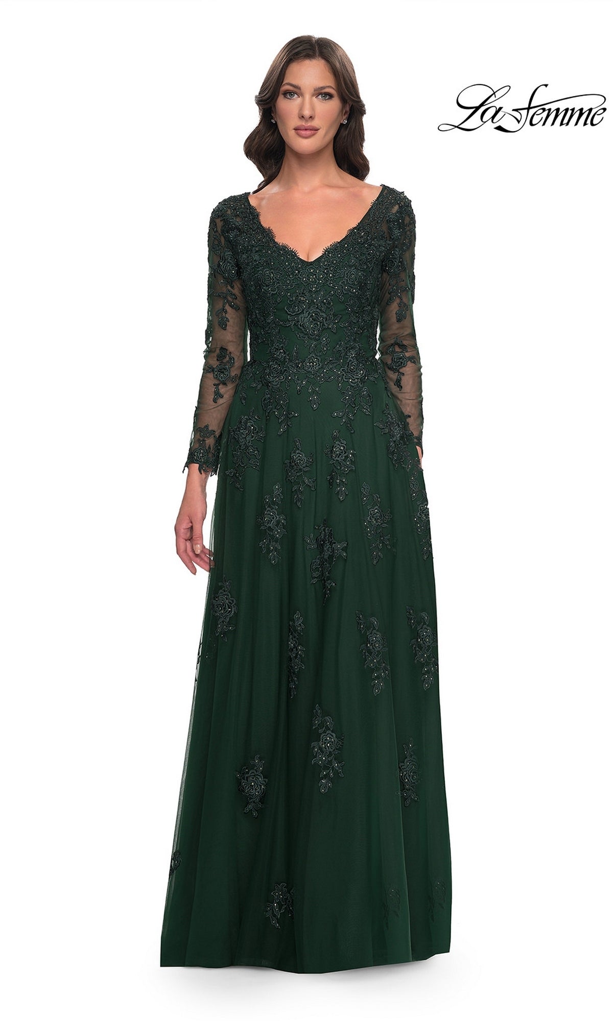A woman wears a La Femme 30795 emerald green V-neck formal gown with sheer sleeves and a tulle A-line skirt detailed with intricate, beaded lace appliques.