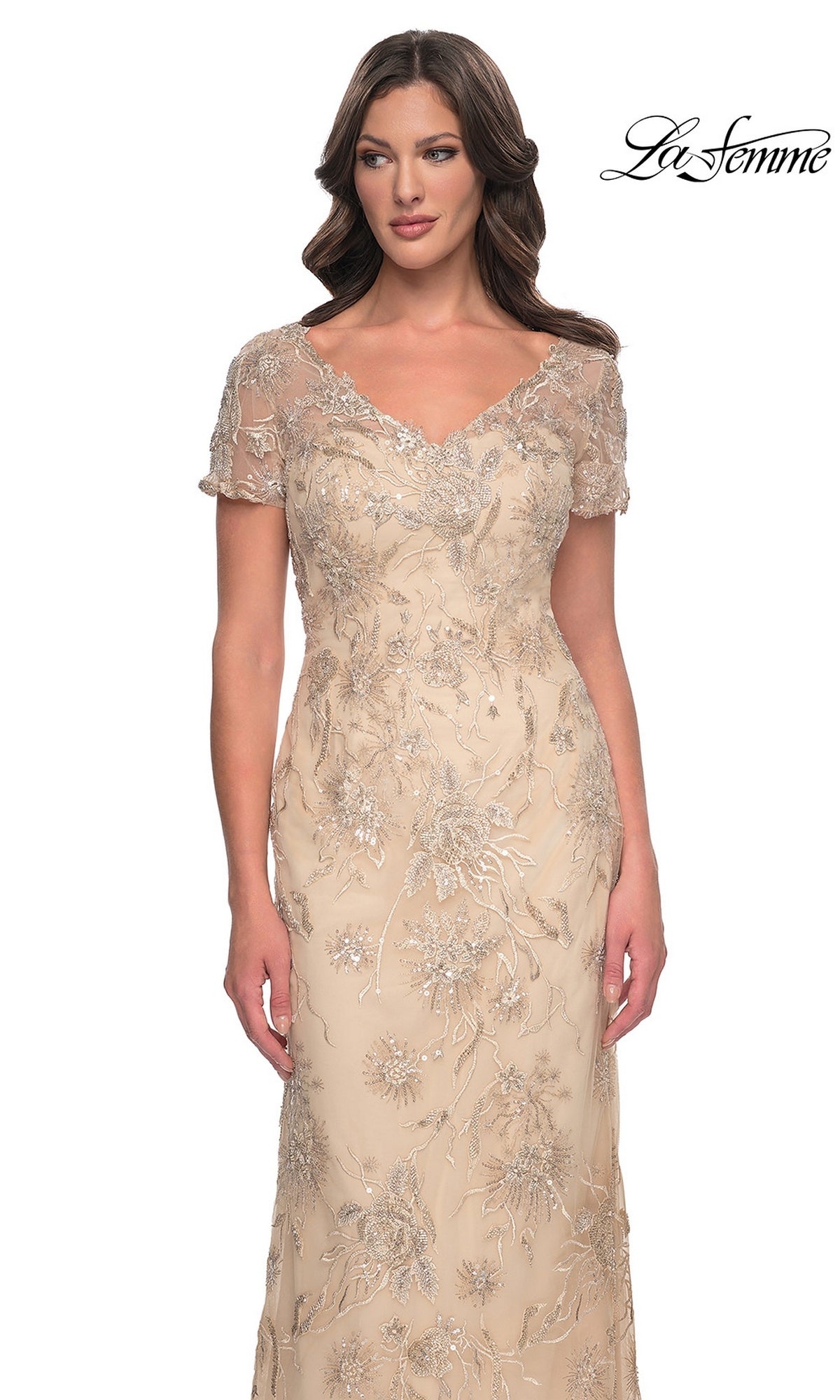 La Femme 30798 is a floor-length, nude-colored V-neck formal dress with short sleeves and intricate silver floral embroidery and sequins.
