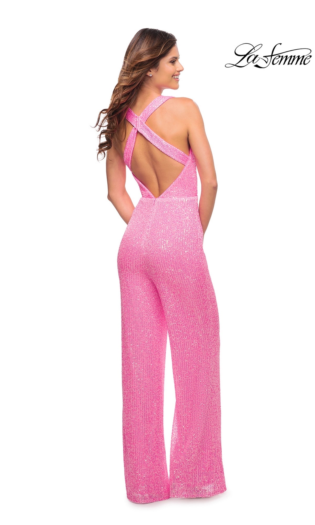 A woman stands facing away in the La Femme Neon Pink Long Sequin Prom Jumpsuit 30811, featuring a crisscross open back. The