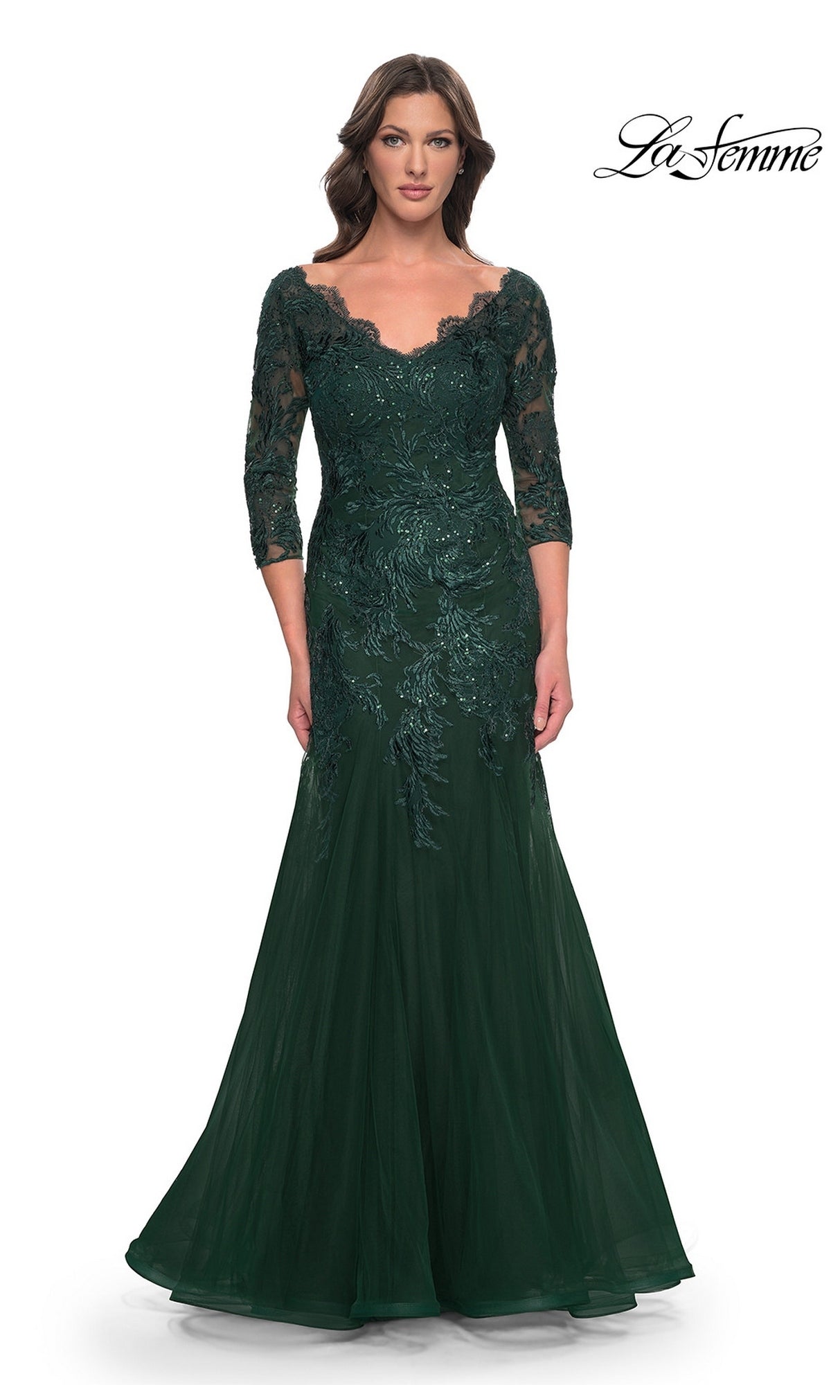 A woman wearing a Long Formal Dress: La Femme 30823, an emerald green modest lace mermaid gown with a floor-length silhouette, three-quarter sleeves, a V-neckline, and sequined floral embroidery.