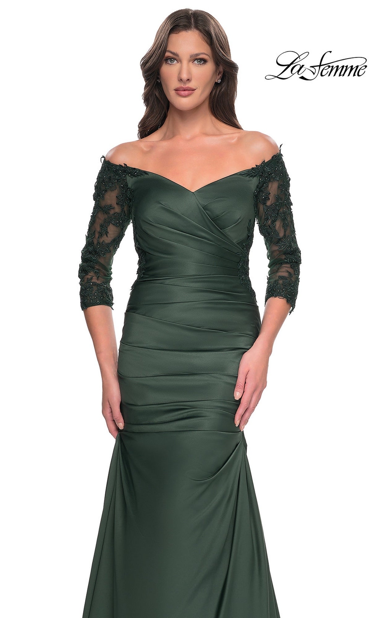 A woman wears the Long Formal Dress: La Femme 30853, a dark green, off-the-shoulder gown with three-quarter length lace sleeves, a ruched bodice, and a trumpet skirt.