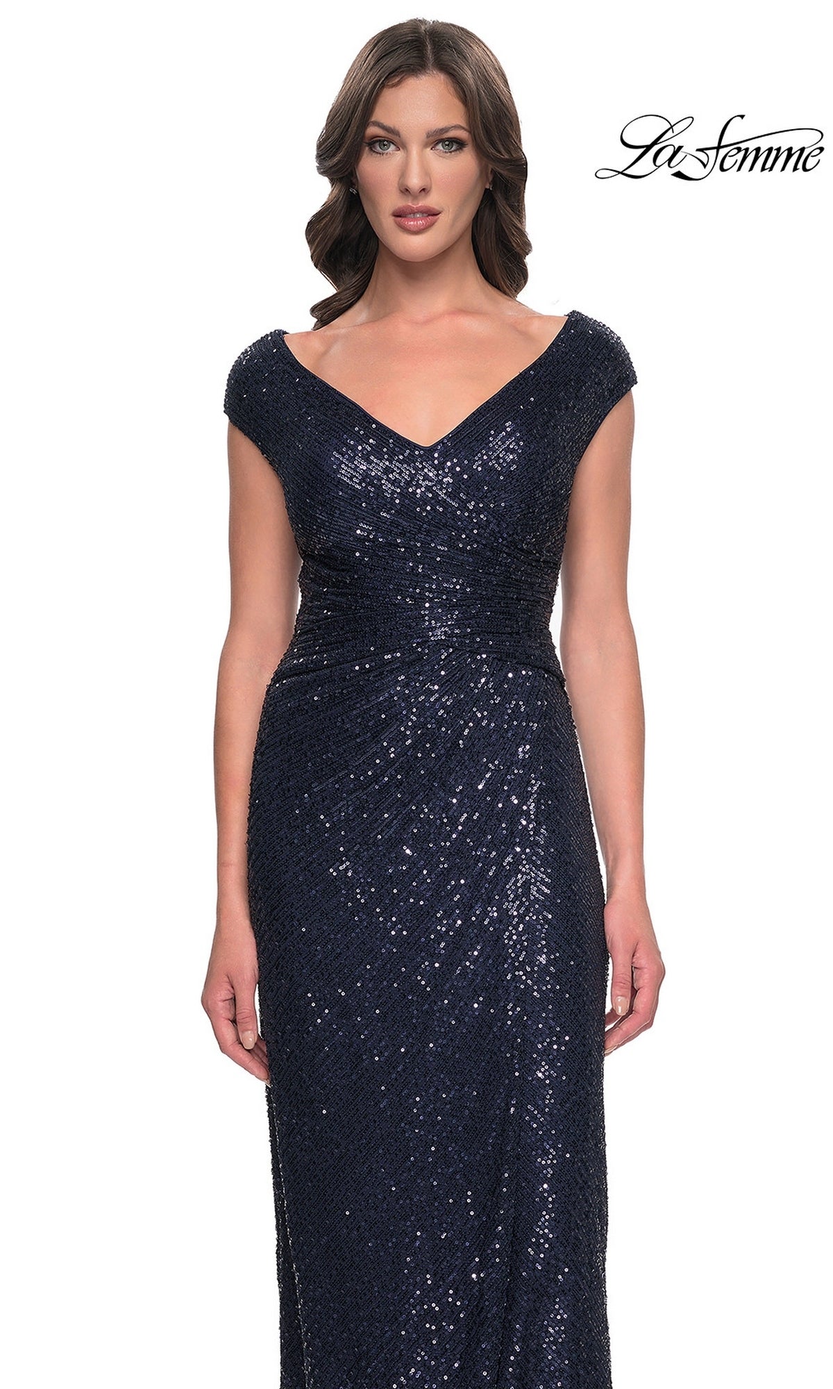A woman wears a navy blue, cap-sleeved, floor-length sequin La Femme 30865 dress with a V-neckline, gathered waist, and sheath silhouette.