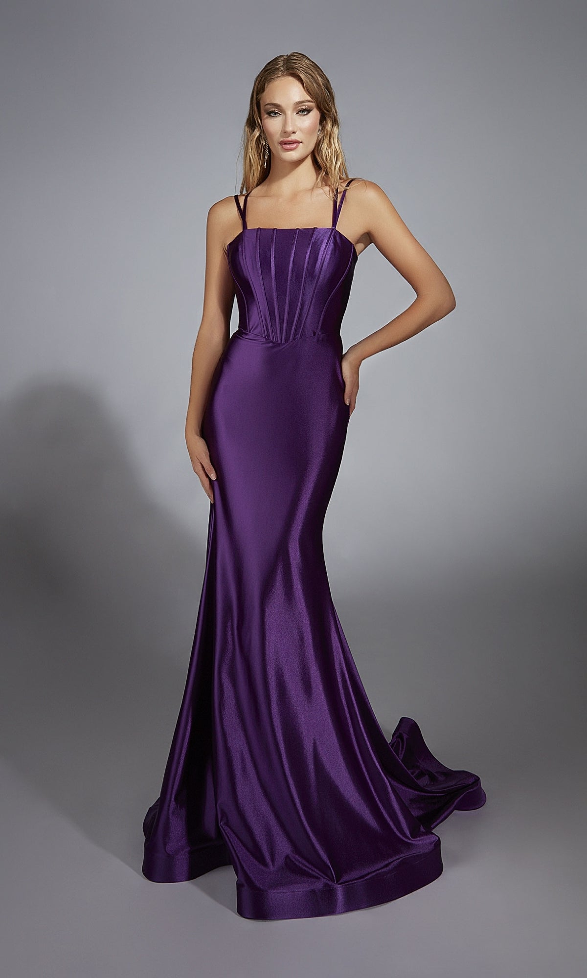 A woman stands against a plain gray background wearing the Aerie Couture 310, an open-back long prom dress featuring a floor-length, sleeveless fitted purple gown with thin straps and a mermaid silhouette.