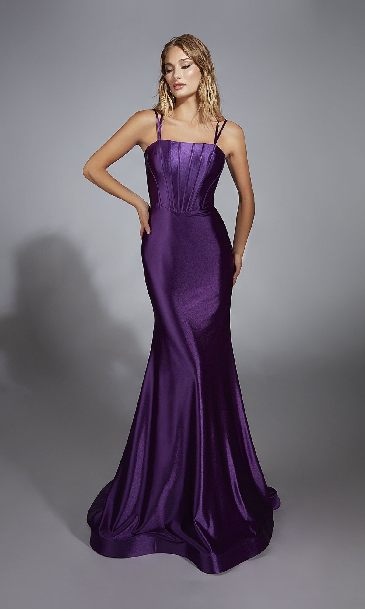 A woman poses against a plain gray background, wearing the Aerie Couture 310 open-back long prom dress—a sleeveless, floor-length gown in purple with a mermaid silhouette and flared hem.