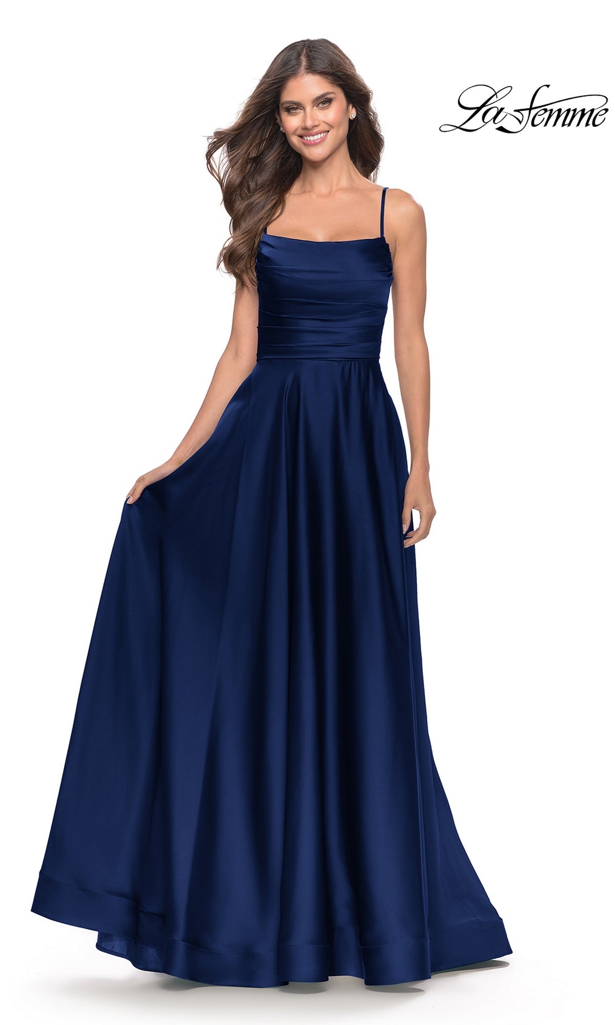 Woman in a sleeveless, floor-length navy Corset-Back La Femme Long A-Line Prom Dress 31105 with a fitted bodice and full skirt, standing and holding the side of her dress.