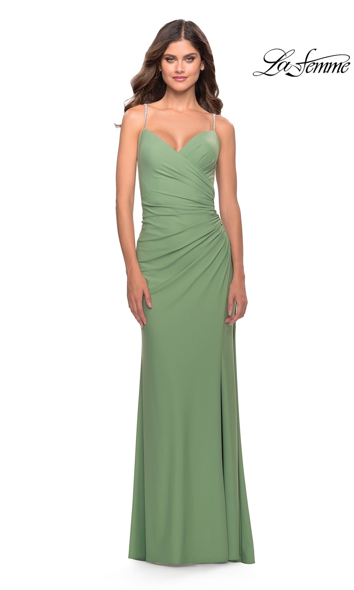 A woman wears the La Femme Wrap-Style Long Prom Dress 31107—a light green, floor-length, sleeveless gown with thin straps and ruched details—standing against a white background. The La Femme logo appears in the top right corner.
