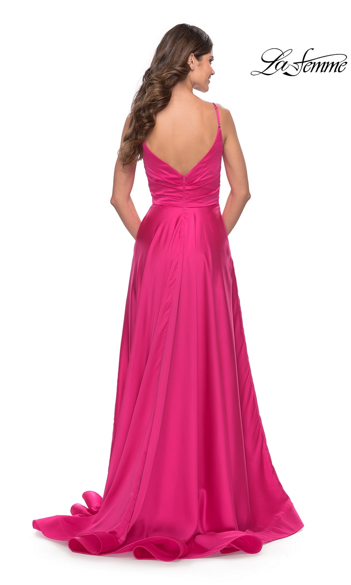 A woman stands facing away, wearing the La Femme Bright Long A-Line Prom Dress 31121—a floor-length, vivid pink gown with thin straps and a deep V-back.