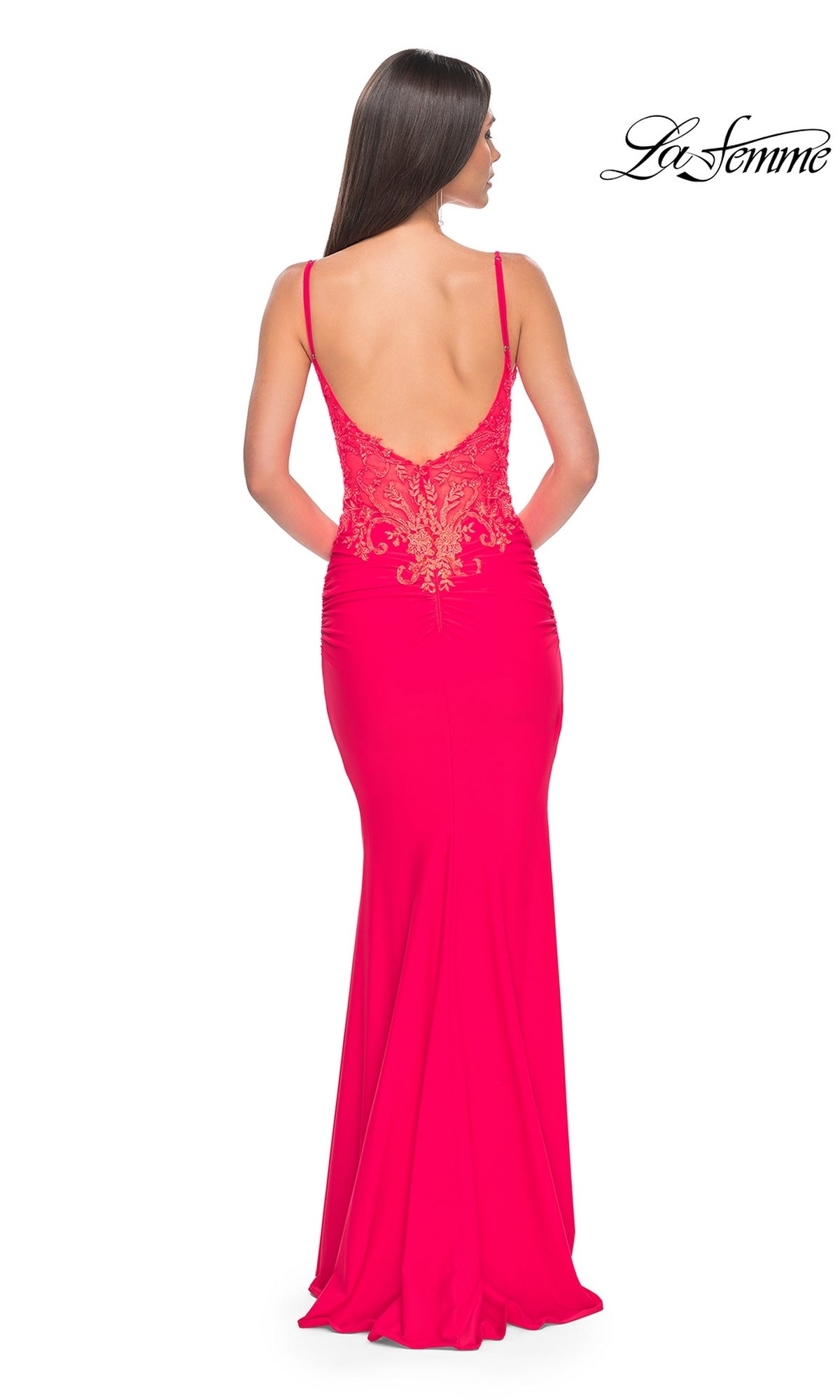 A woman wears the La Femme Sheer-Waist Long V-Neck Prom Dress 31128, a bright pink gown with thin straps, an open back, and an embroidered lace bodice with gold detailing. The La Femme logo appears in the top right corner.