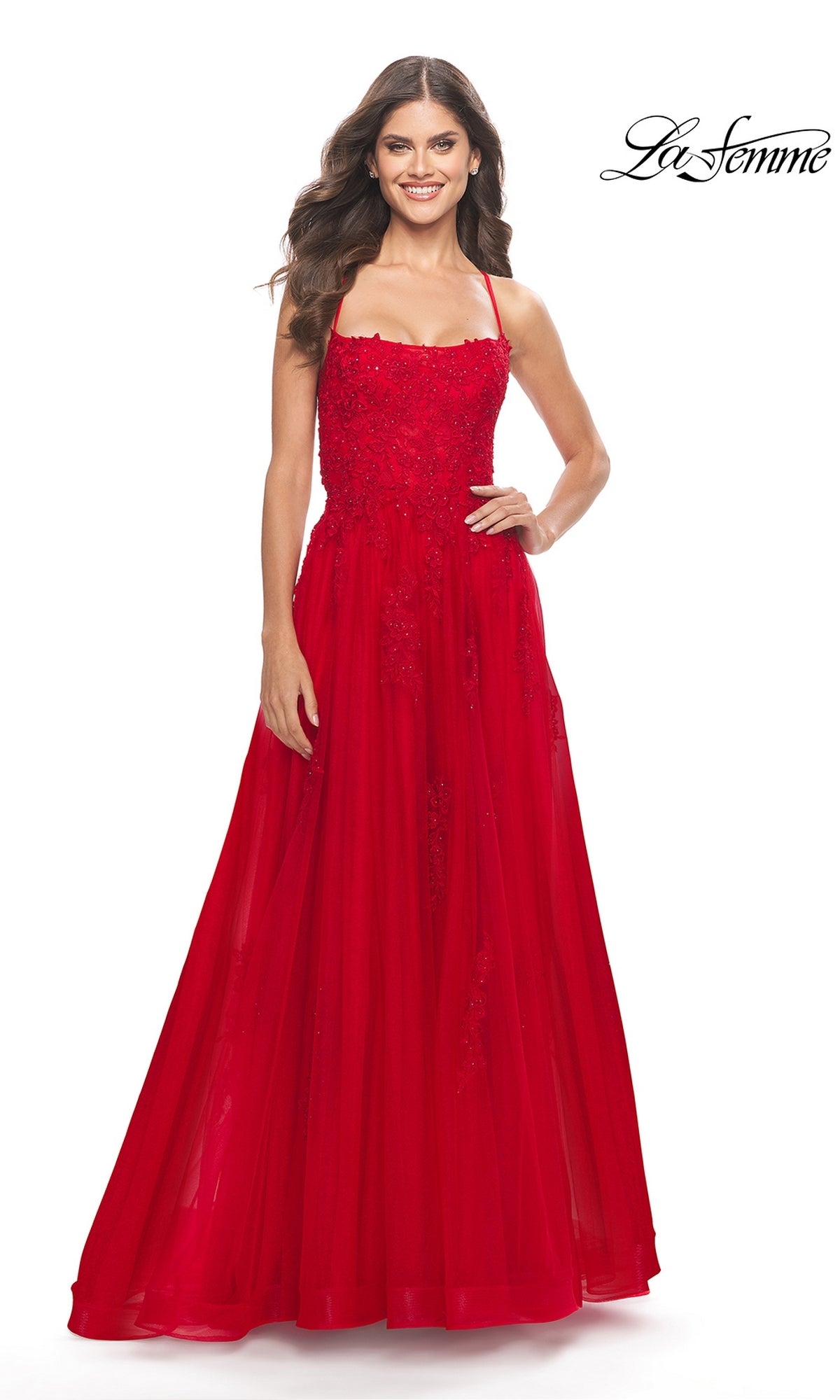 A woman stands and smiles against a plain white background in the La Femme Long A-Line Lace Prom Ball Gown 31135, a sleeveless, floor-length red dress with beaded details. The La Femme logo appears in the top right corner.