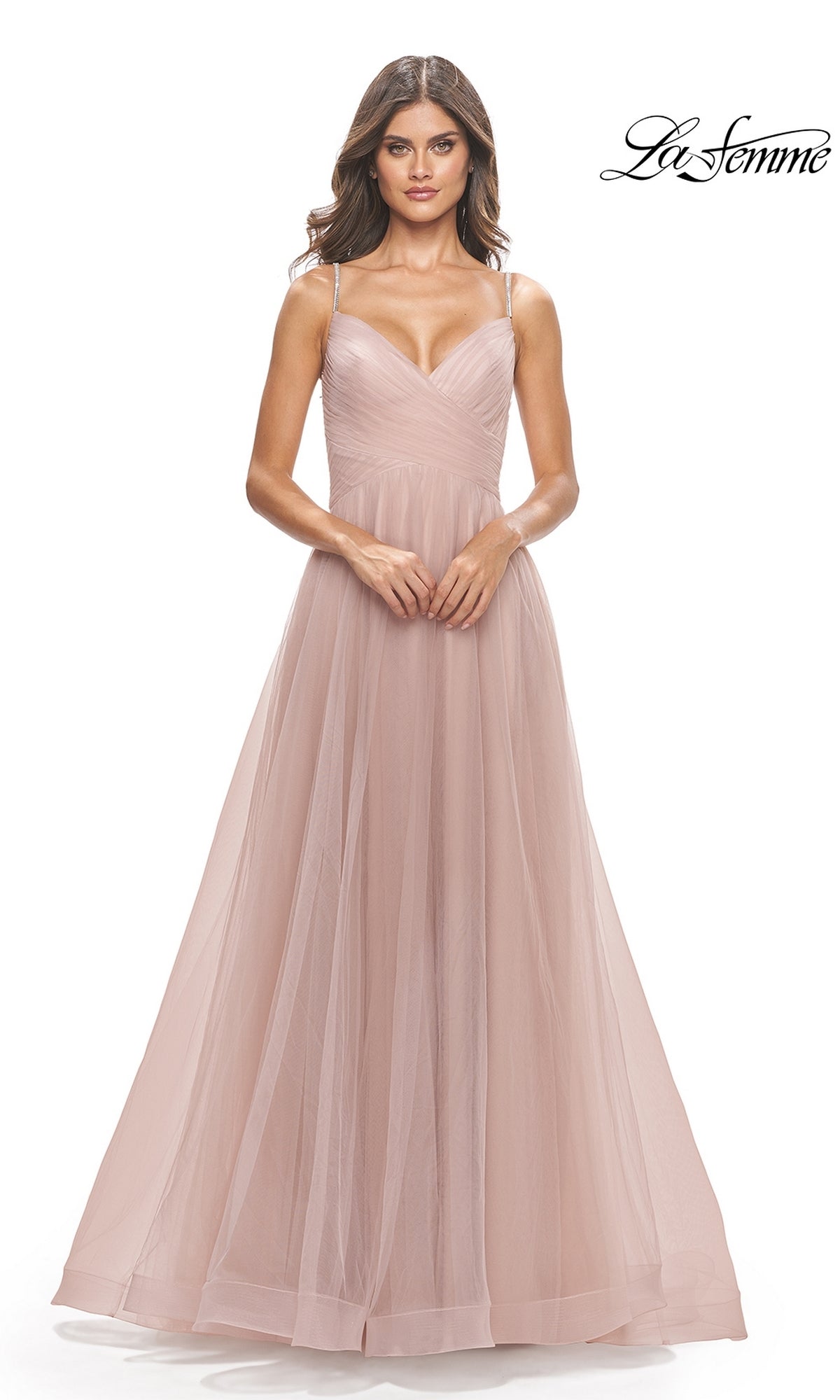 A woman wears the La Femme A-Line Long Tulle Prom Dress 31204 in blush pink, a floor-length gown with spaghetti straps, standing against a white background.