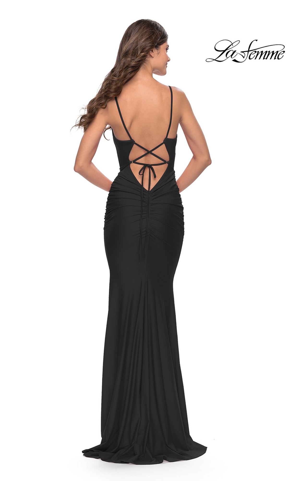 Woman wearing the Simple V-Neck La Femme Designer Prom Dress 31227, a long black fitted gown with thin straps, ruching, and a lace-up open back, poses facing away from the camera.