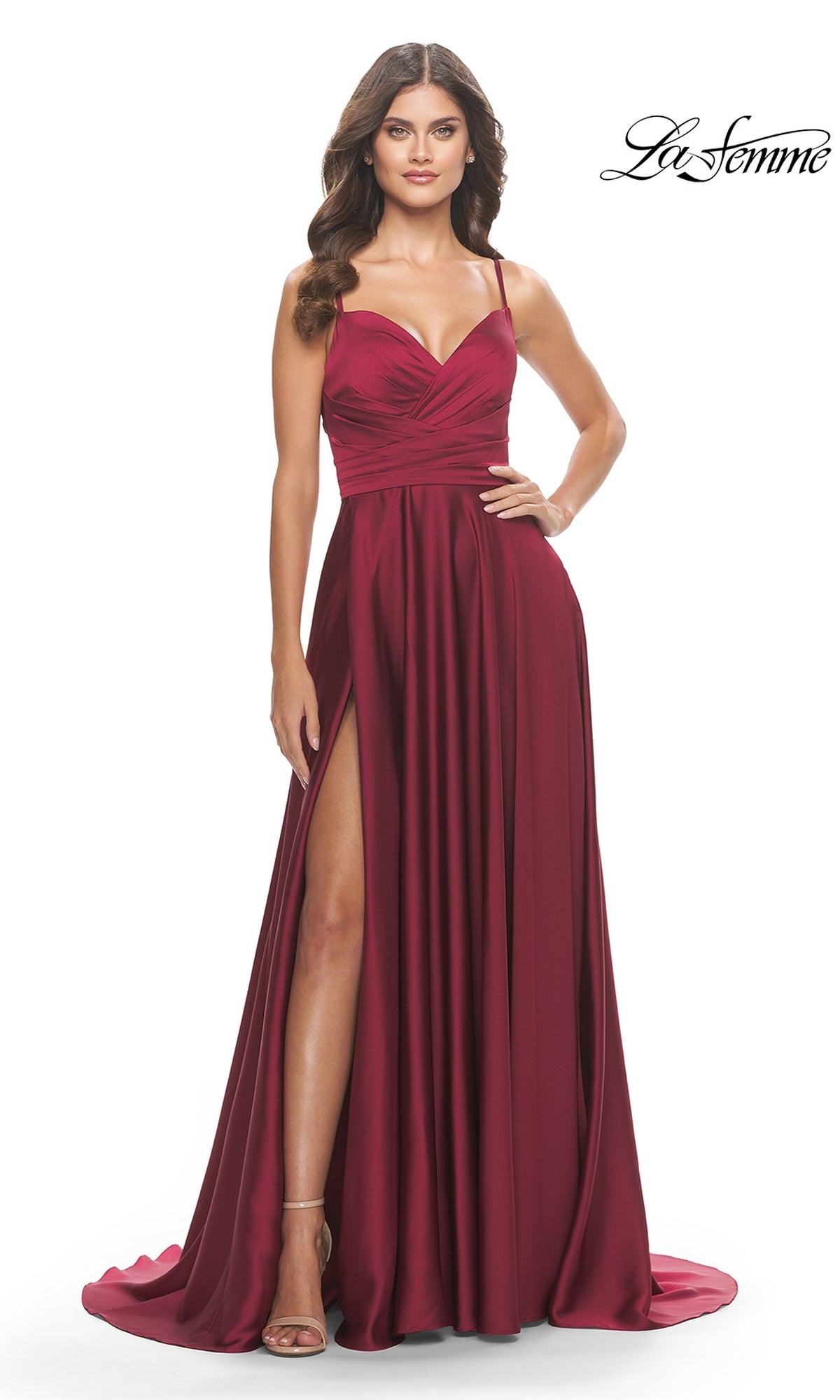 A woman stands against a white background in the La Femme Open-Back A-Line Designer Prom Dress 31233, a sleeveless, floor-length burgundy gown with spaghetti straps, ruched bodice, and thigh-high slit.