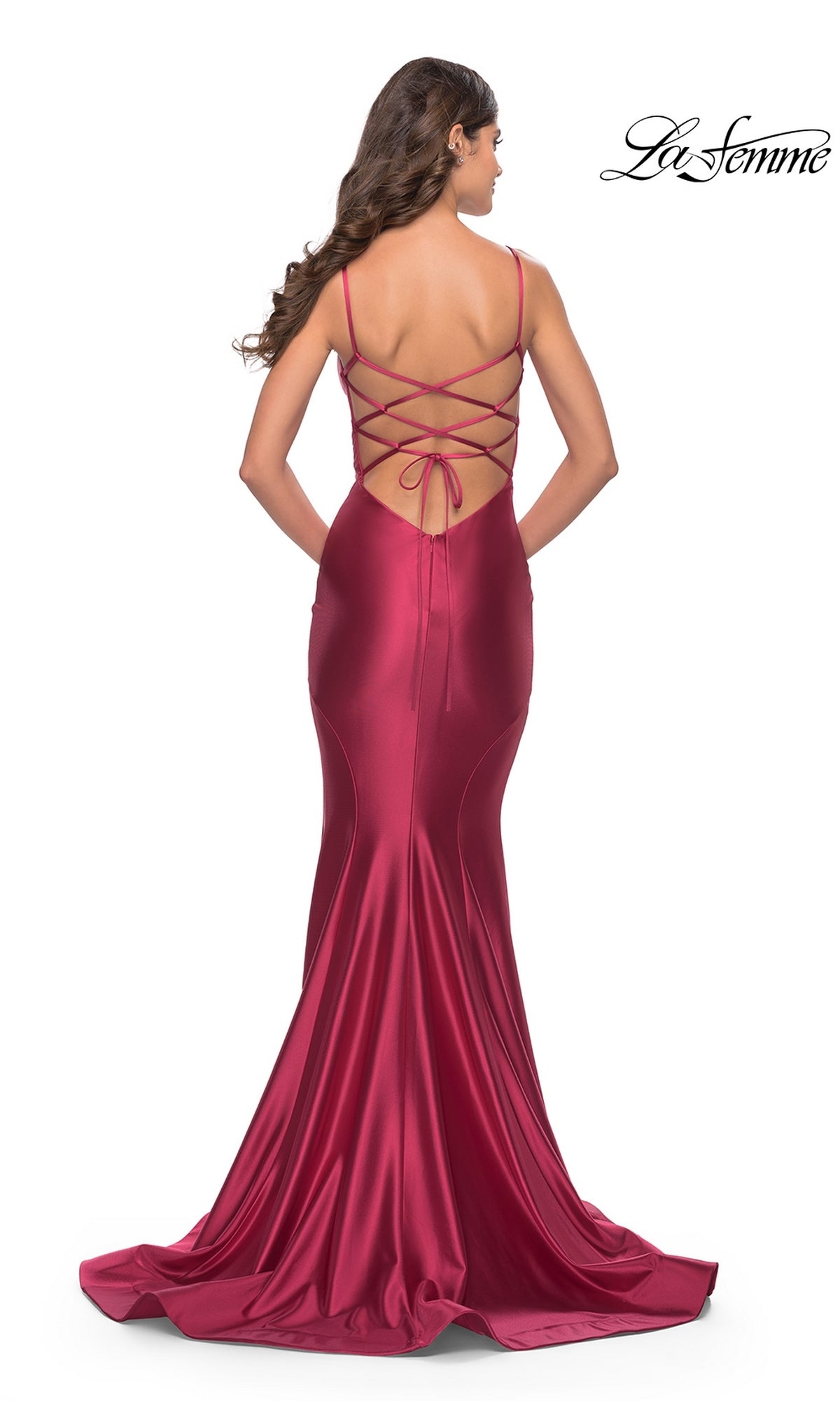 A woman wears the La Femme Lace-Up Open-Back Long Prom Dress 31295, featuring a floor-length deep red satin, thin straps, lace-up open back, and a mermaid skirt as she stands facing away from the camera.