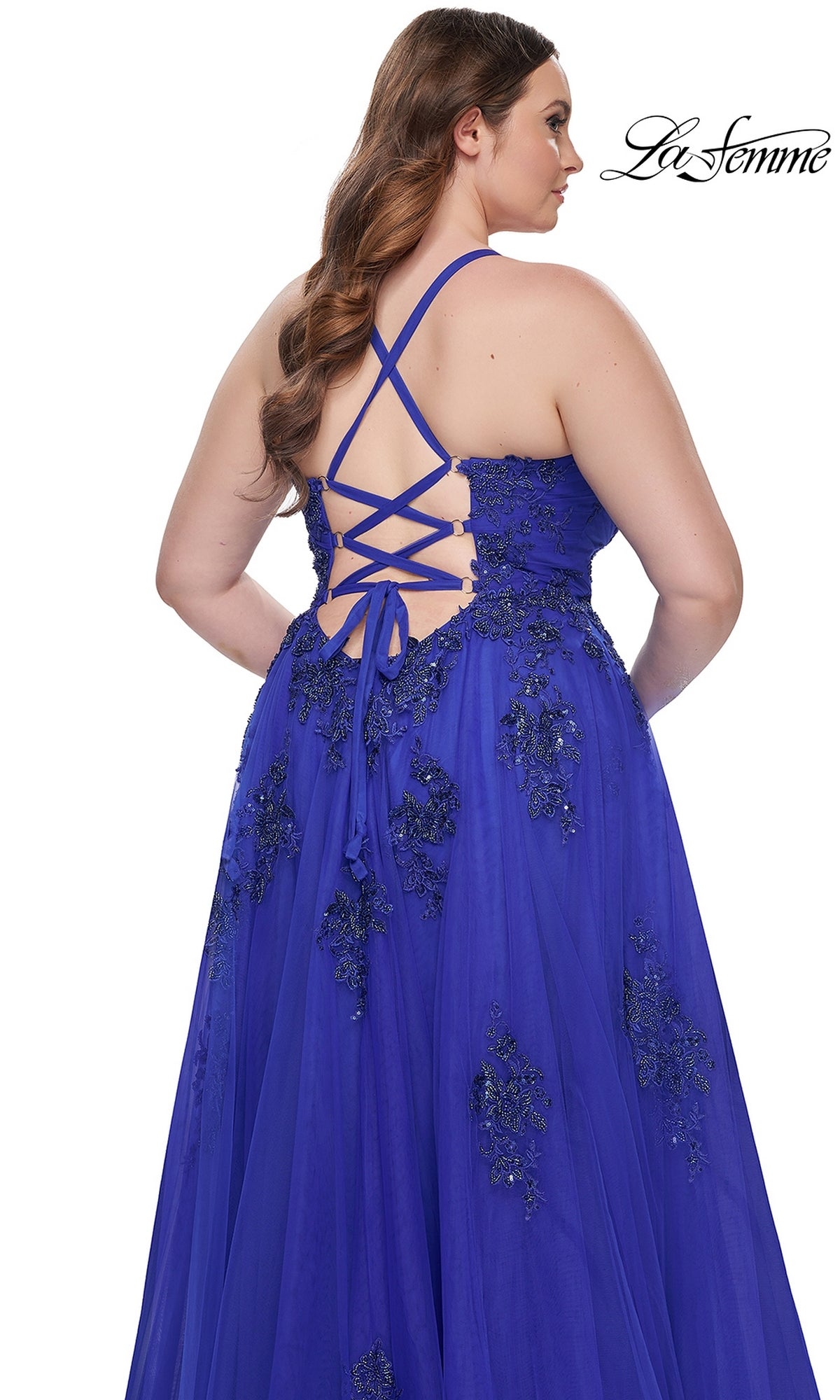 A woman wearing the La Femme Long Prom Dress 31378—a plus-size, royal blue gown featuring embroidered lace, a sleeveless bodice, crisscross lace-up back, and a flowing floor-length skirt.